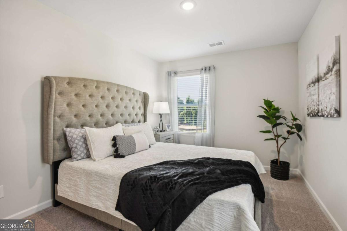 Staged bedroom with a tufted beige headboard, white bedding, black throw, and potted plant.