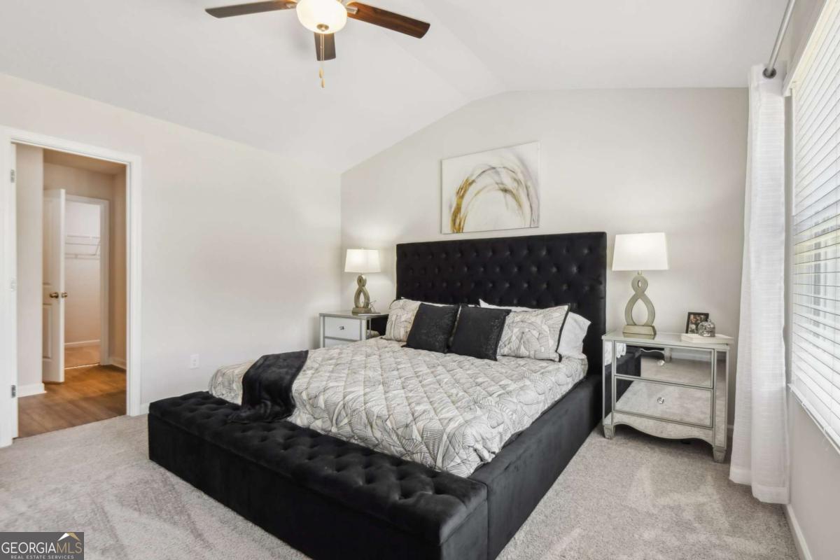 Staged bedroom with a black upholstered bed, mirrored nightstands, and a ceiling fan.
