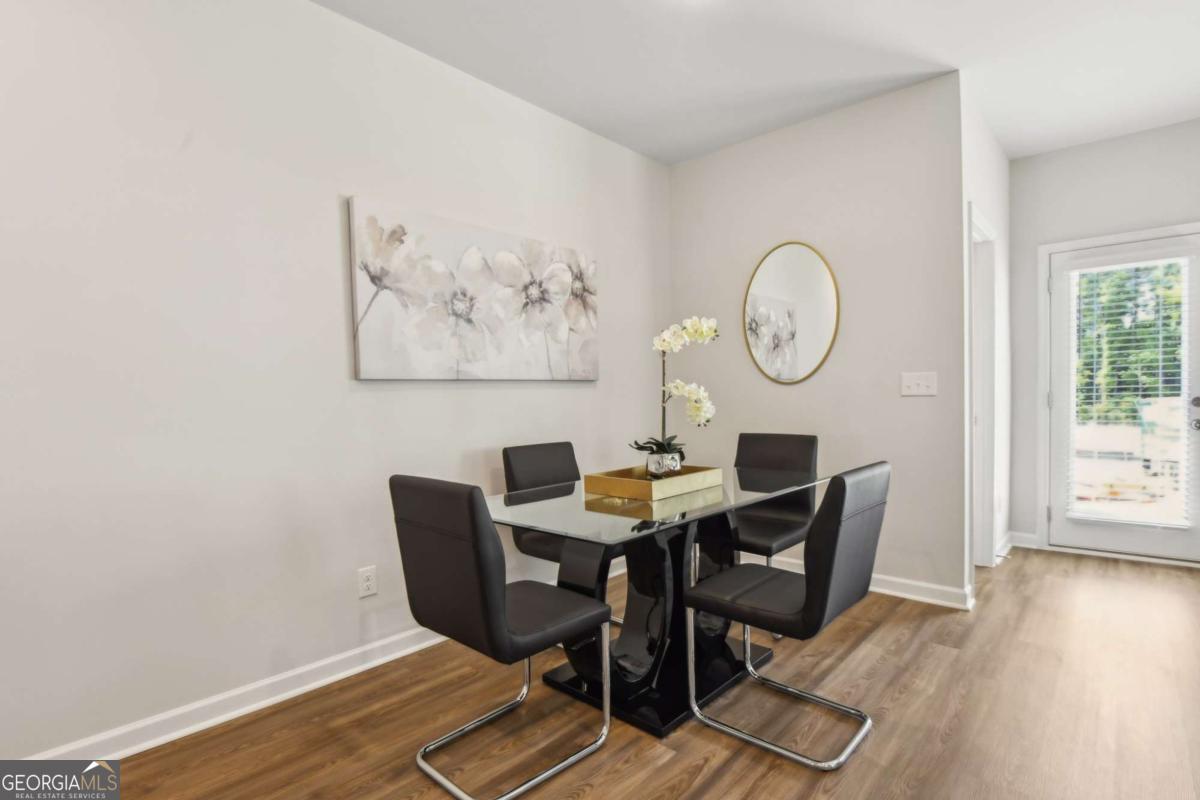 Dining area with a glass-top table, four dark chairs, floral art, and a round mirror.