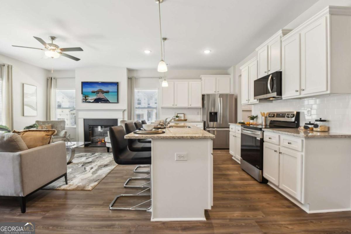 Open kitchen and living area with a granite island, white cabinets, stainless appliances, and a fireplace.