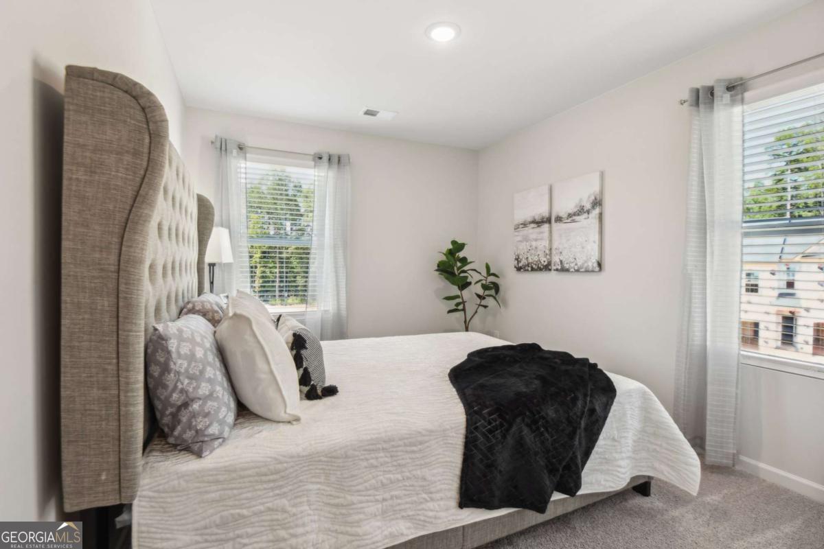 Furnished bedroom with a tall tufted headboard, white bedding, and windows with sheer curtains.