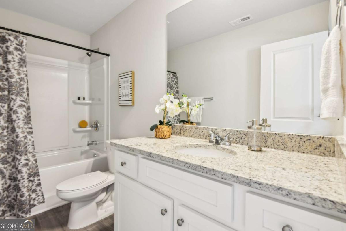 Bathroom with a long speckled granite vanity, large mirror, and white tub-shower.