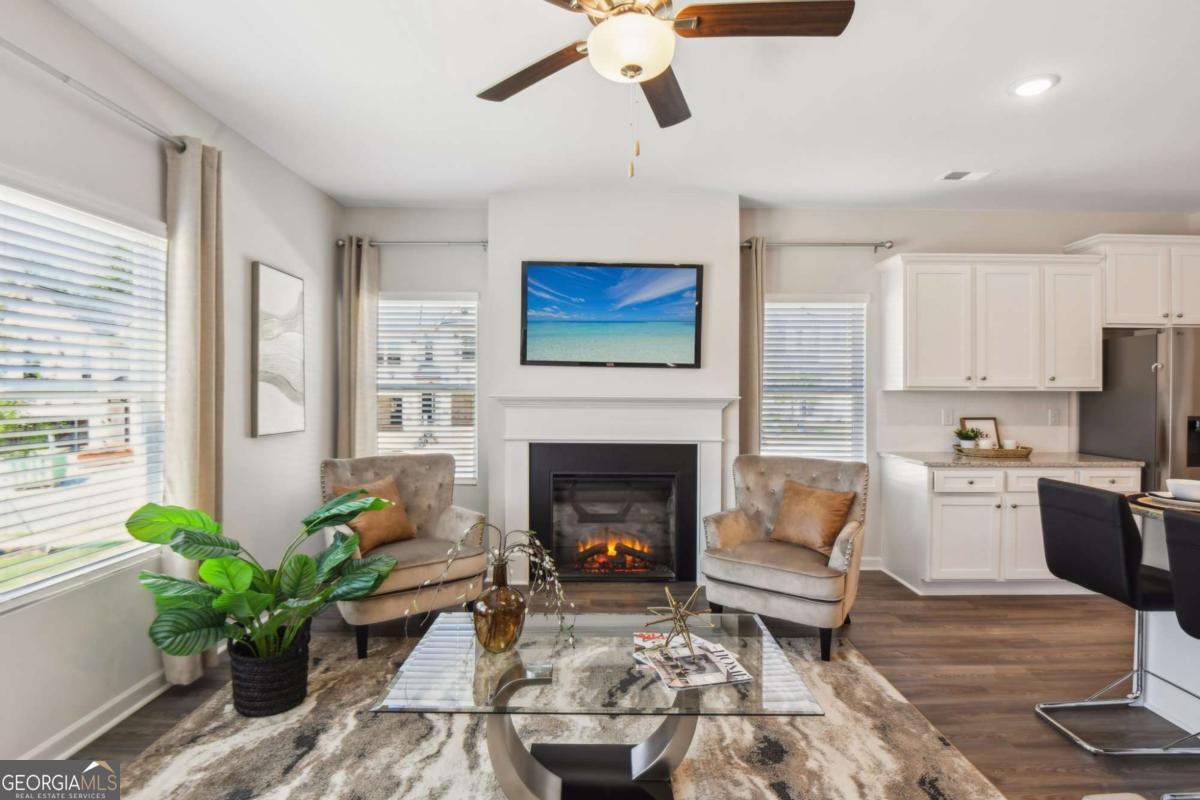 Living room with a fireplace, two armchairs, and an open white-cabinet kitchen.