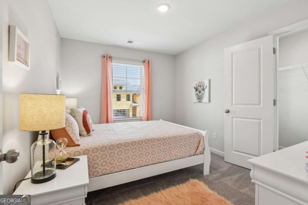 Staged bedroom with a floral bedspread, coral curtains, gray carpet, and an open closet.
