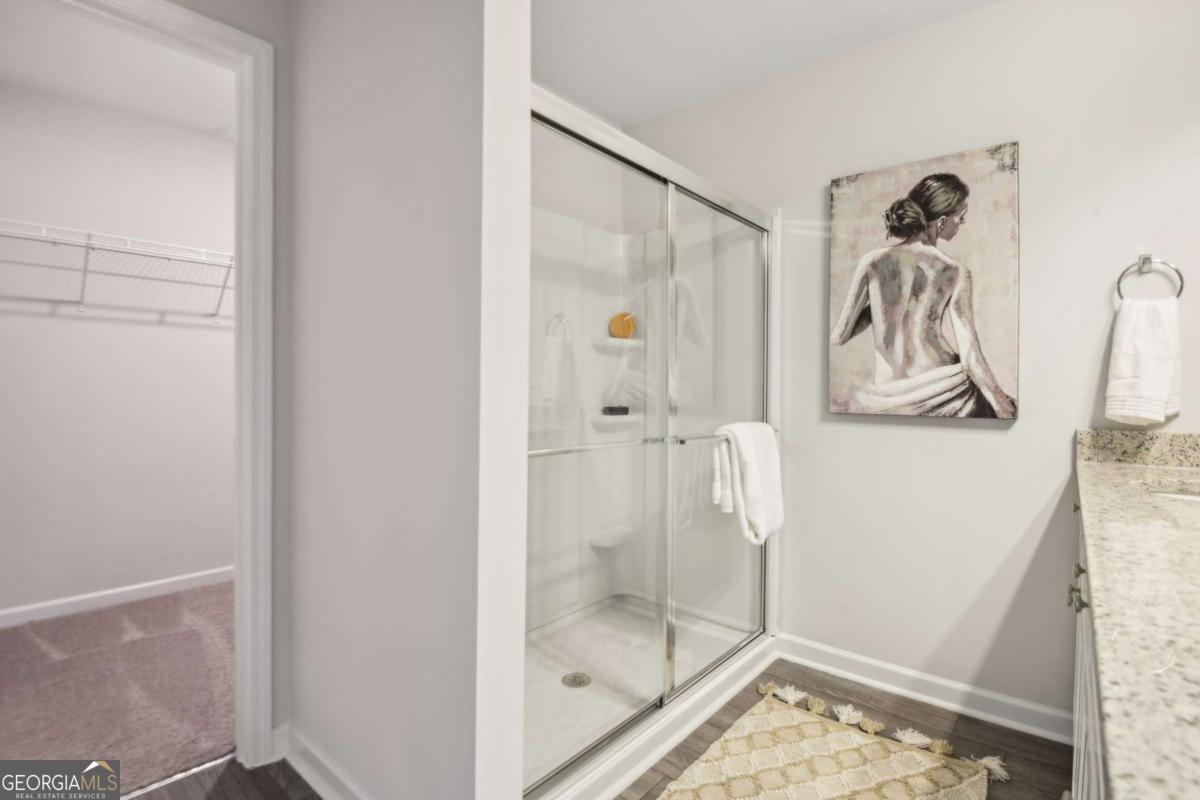 Bathroom with a glass-enclosed shower, granite vanity, and doorway to a carpeted walk-in closet.