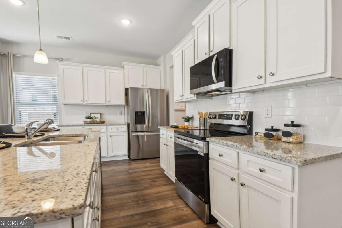 Kitchen with white cabinetry, granite counters, stainless steel appliances, and dark wood floors.
