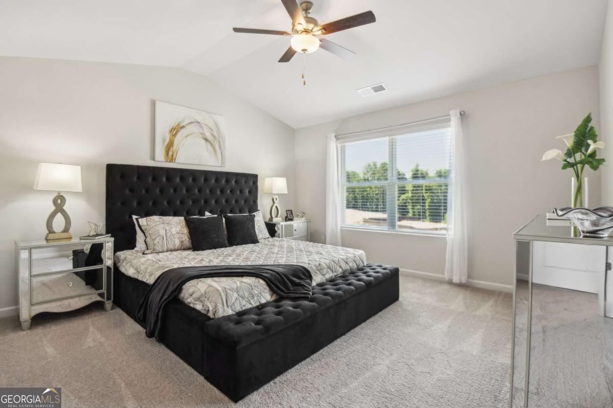Primary bedroom with a black tufted bed, upholstered bench, and large window overlooking greenery.
