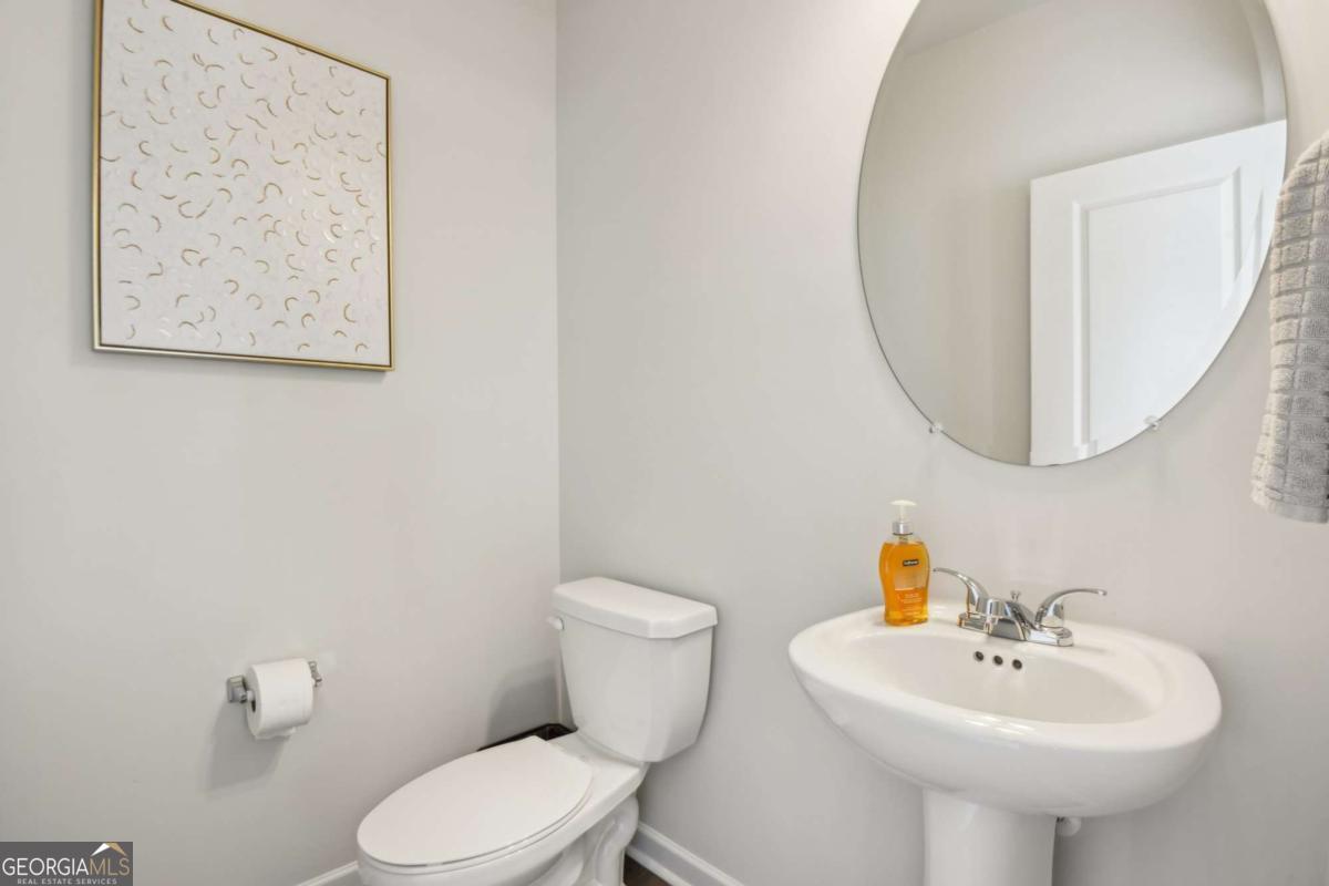 Bathroom with a white toilet, pedestal sink, large round mirror, and framed abstract artwork.