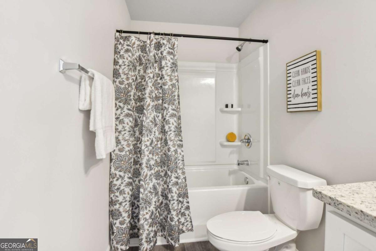 Bathroom with a floral shower curtain, white tub and toilet, and granite vanity countertop.