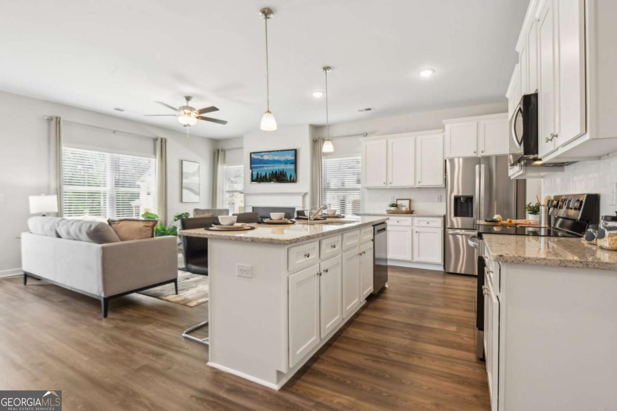 Open-plan kitchen with a large granite island, white cabinetry, stainless appliances, and an adjoining living area.