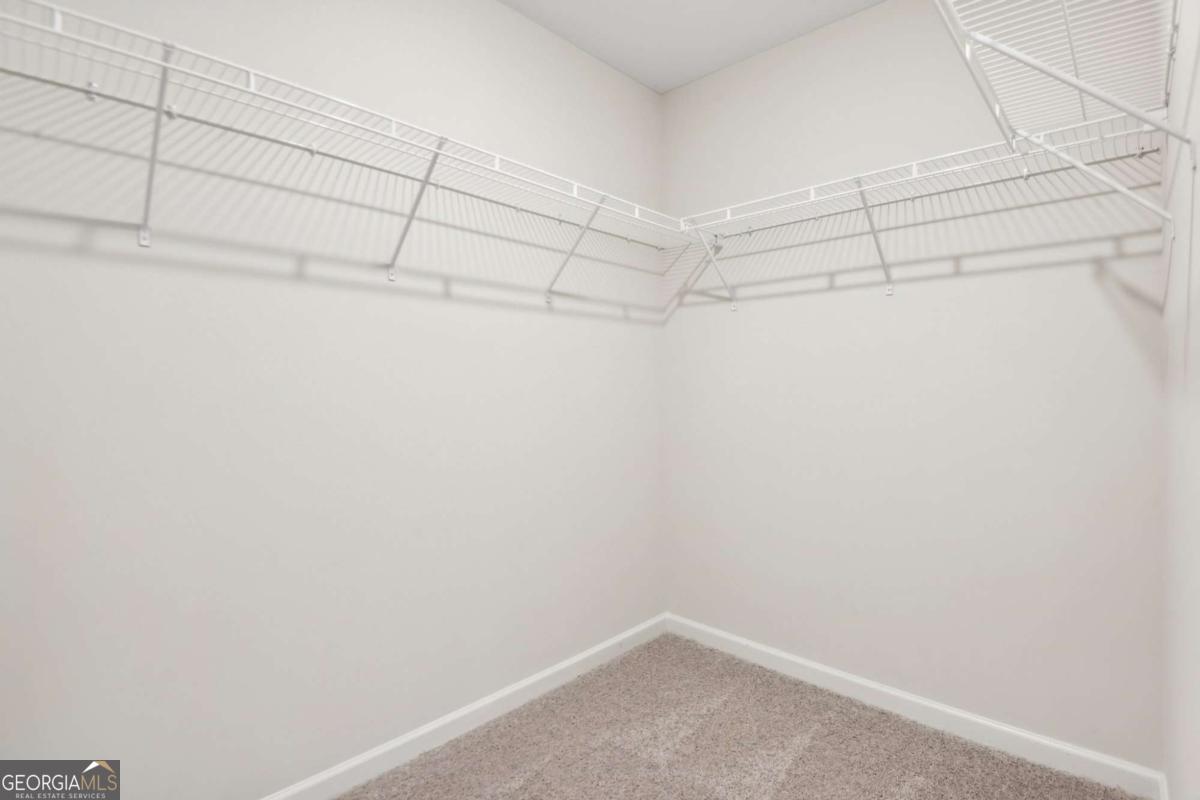 Empty walk-in closet with wraparound white wire shelving and beige carpet.