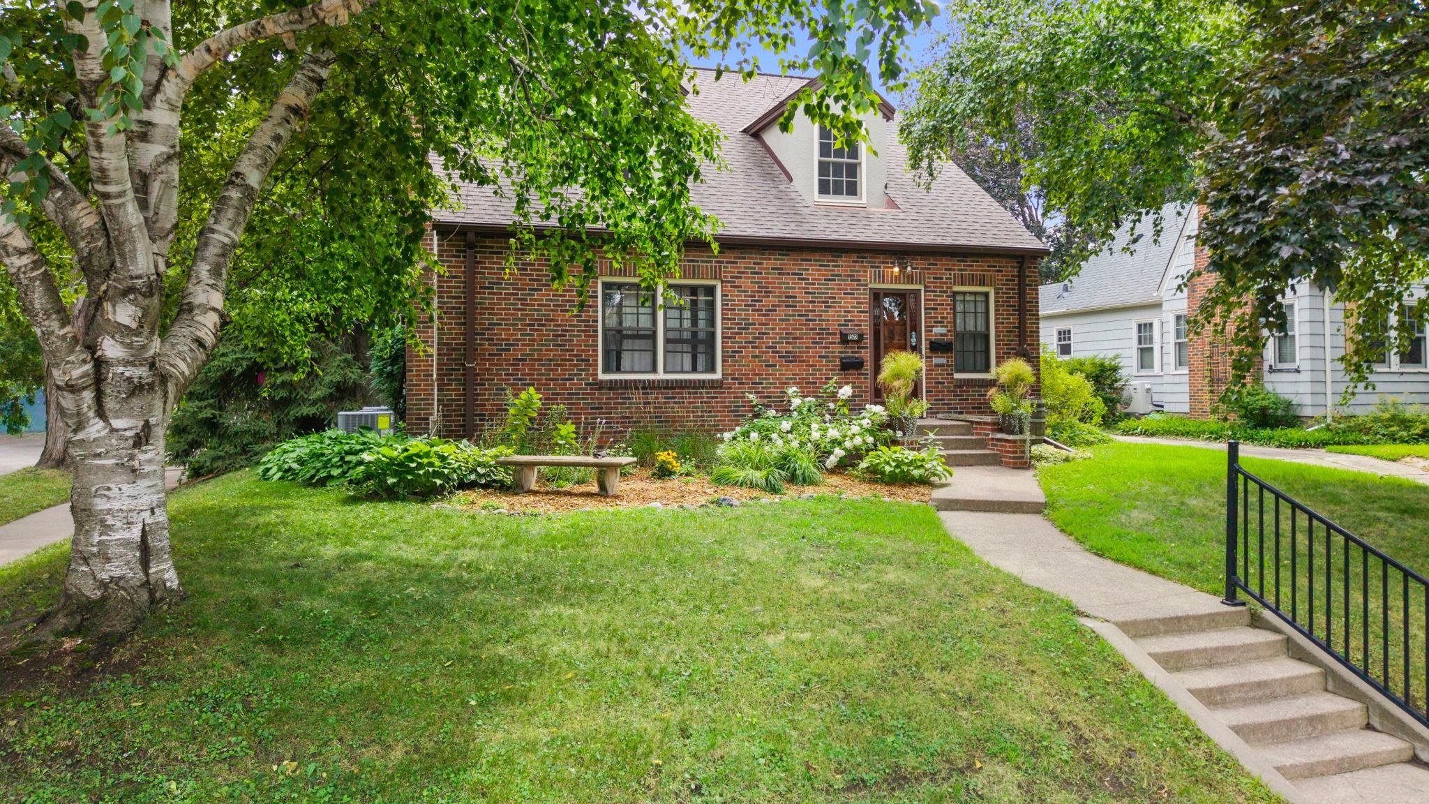 Red brick house with a dormer, landscaped front garden, and mature trees.