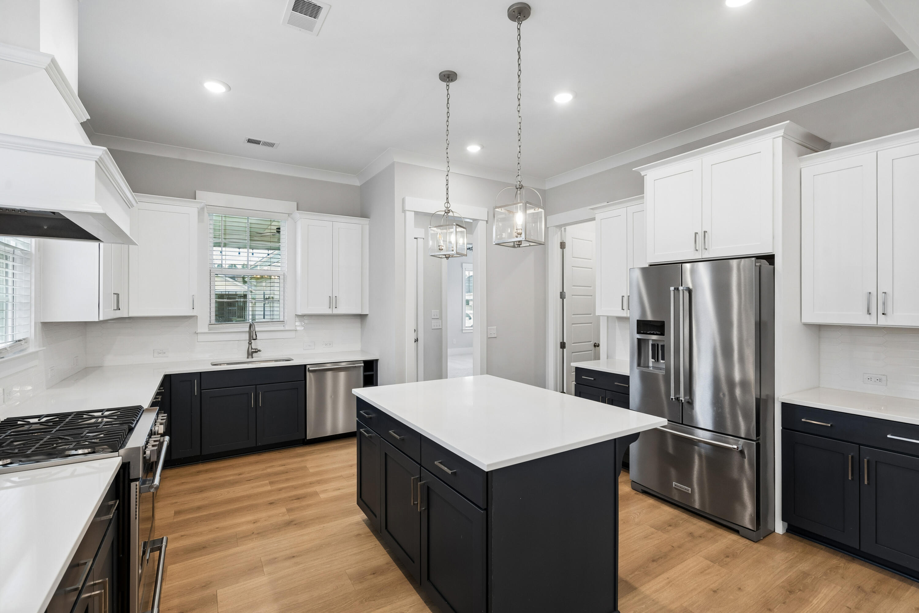 Kitchen with a large dark-cabinet island, white countertops, stainless appliances, and warm wood flooring.