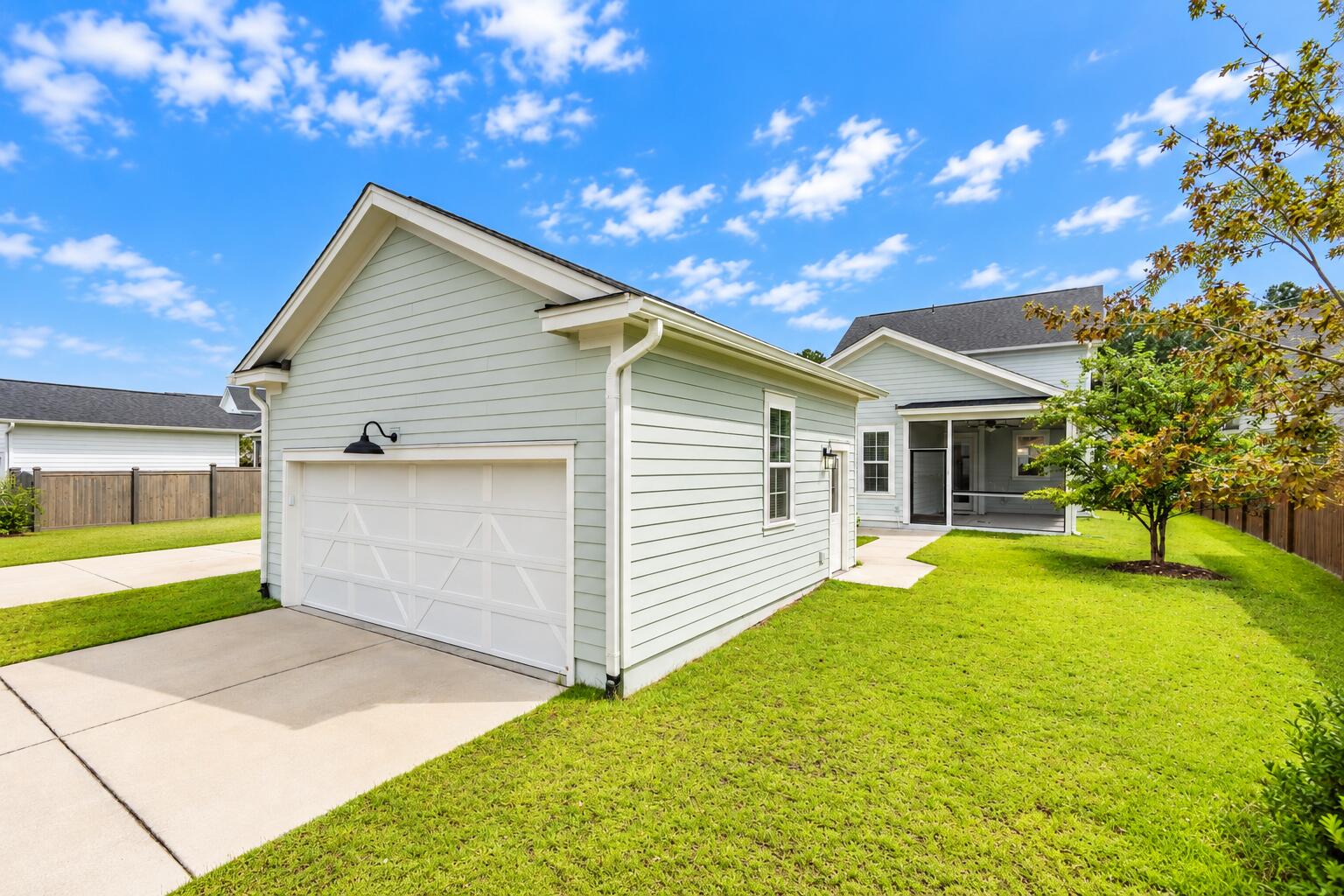 Light gray-green home with a white double garage, covered patio, and broad green lawn.