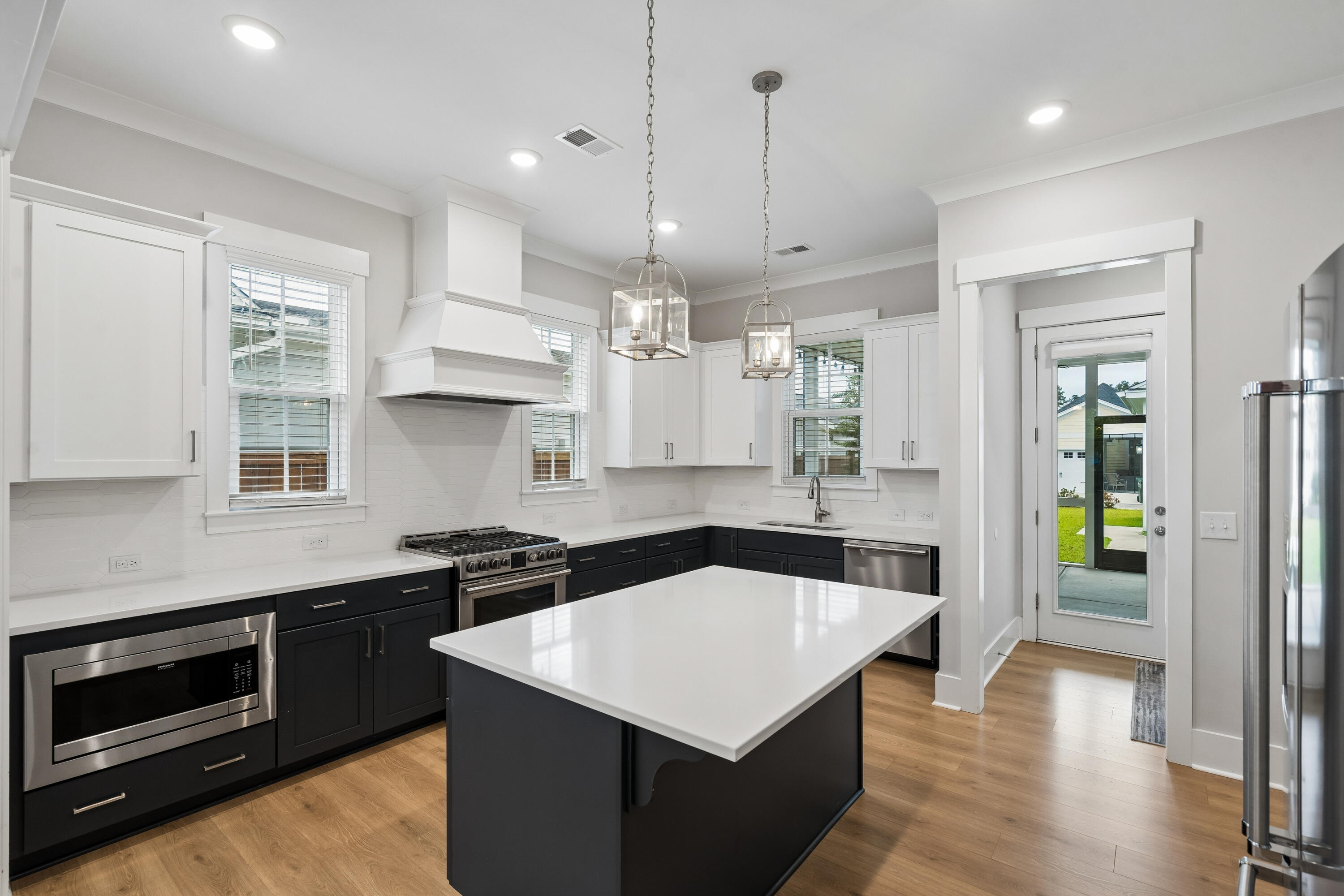 Kitchen with a large white island, dark cabinets, stainless steel appliances, and a glass door to the backyard.