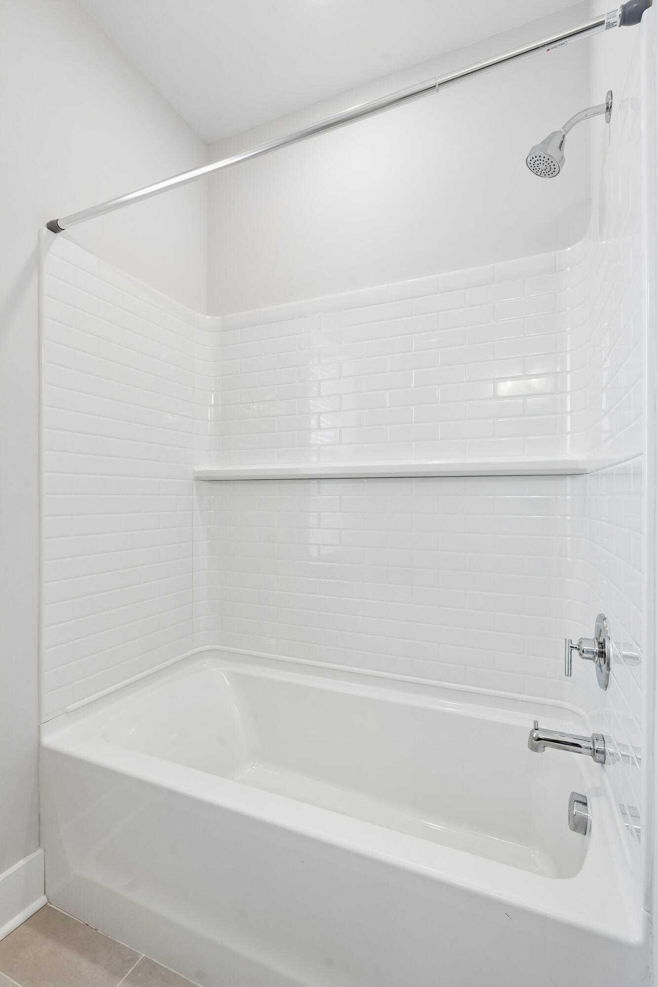White bathtub and shower with subway tile, chrome fixtures, and a built-in ledge.