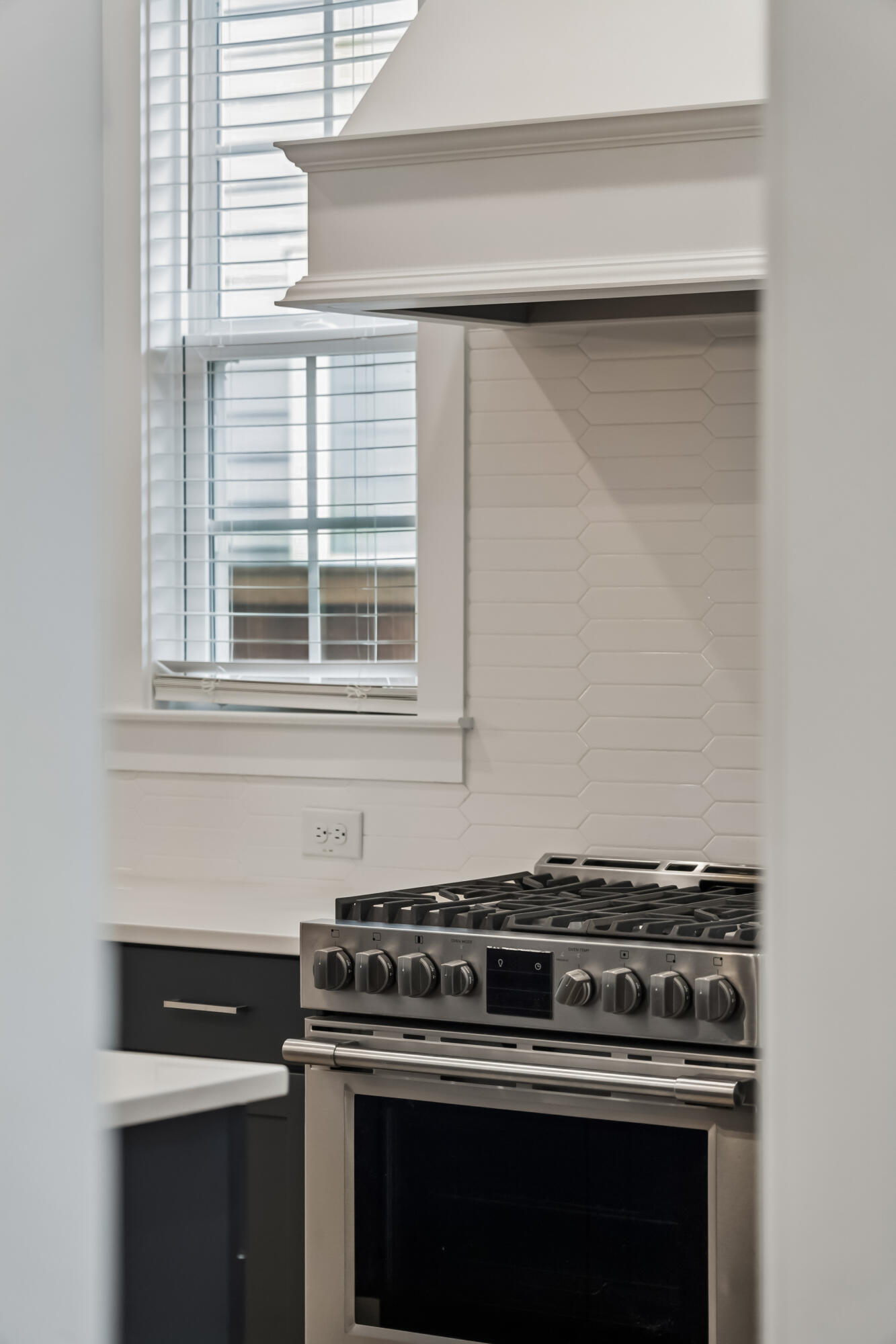 Kitchen range beneath a white hood, with hexagonal tile backsplash and a shuttered window.