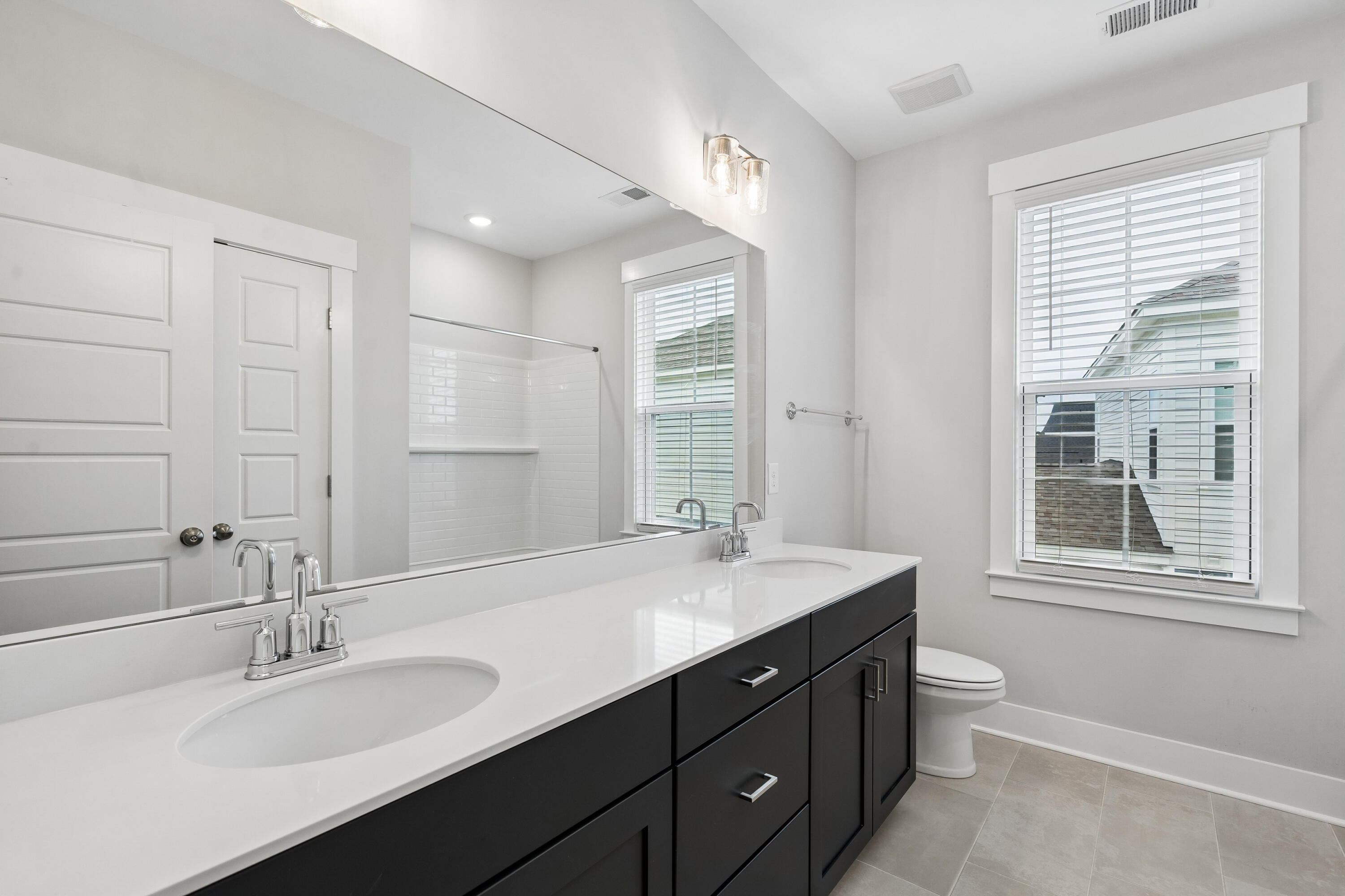 Bathroom with a dark double vanity, white countertop, mirrored wall, and tiled shower.