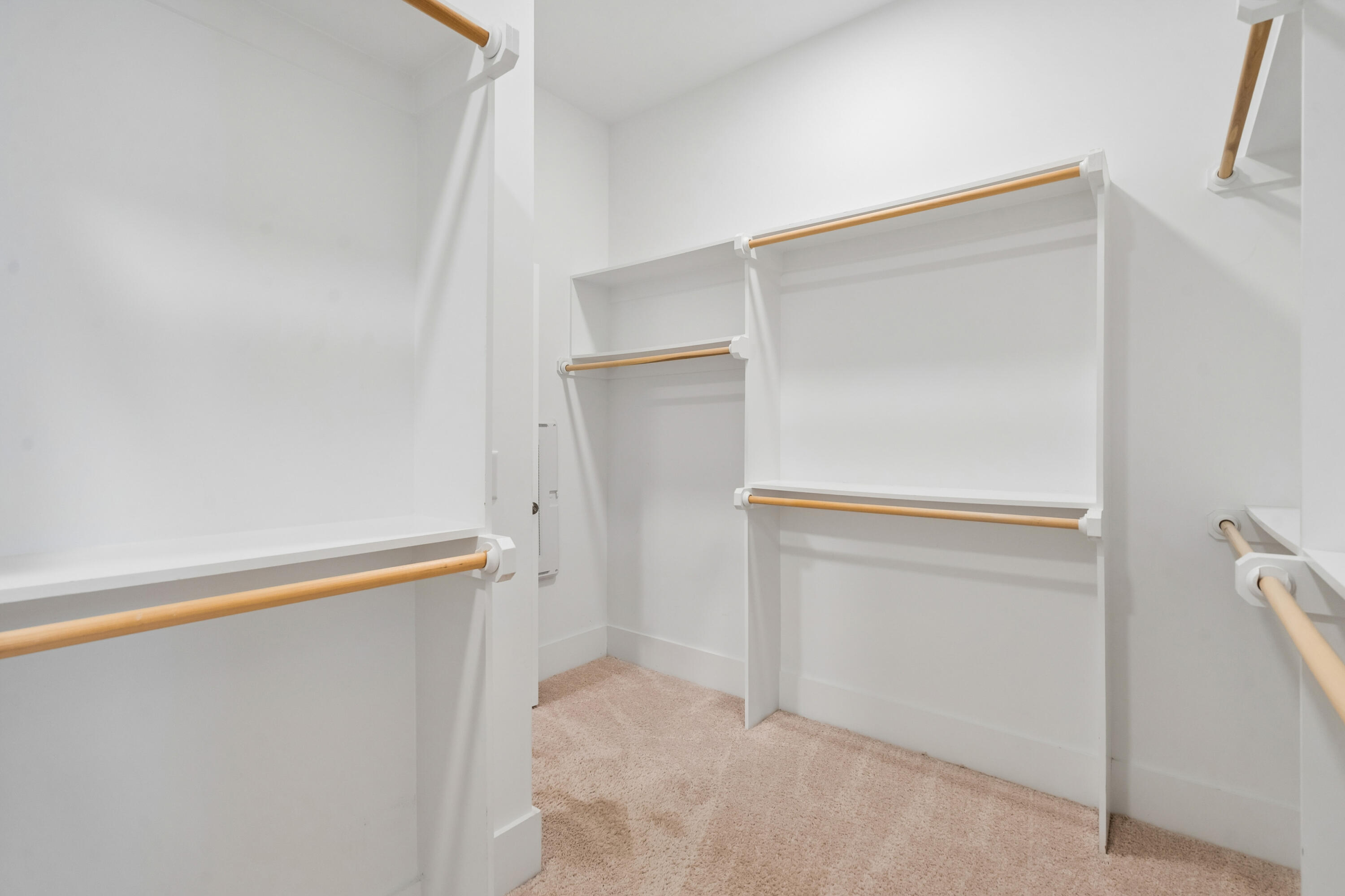Walk-in closet with white built-in shelving, multiple wood hanging rods, and beige carpet.