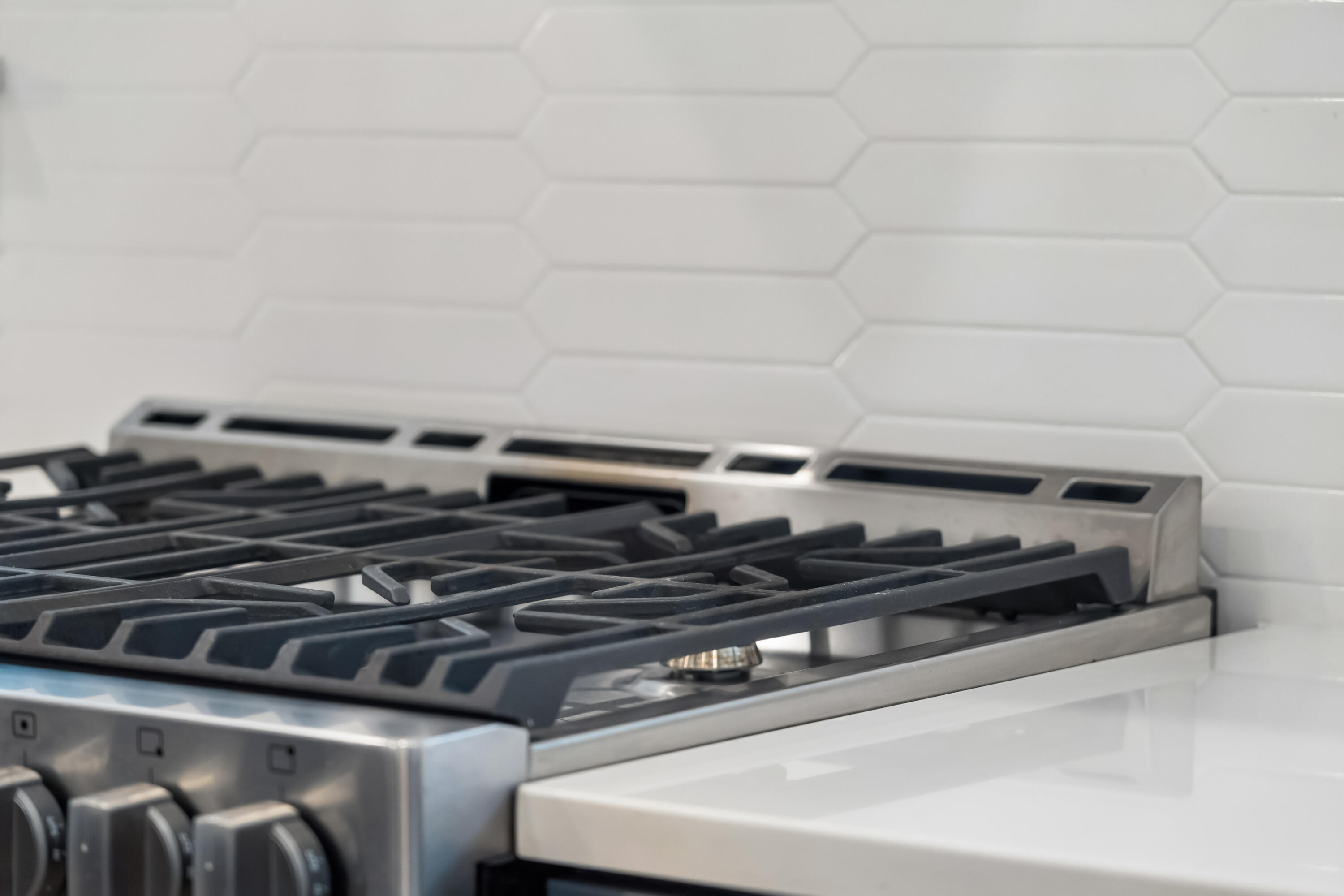 Stainless steel gas range with black grates beneath a white elongated hexagon tile backsplash.