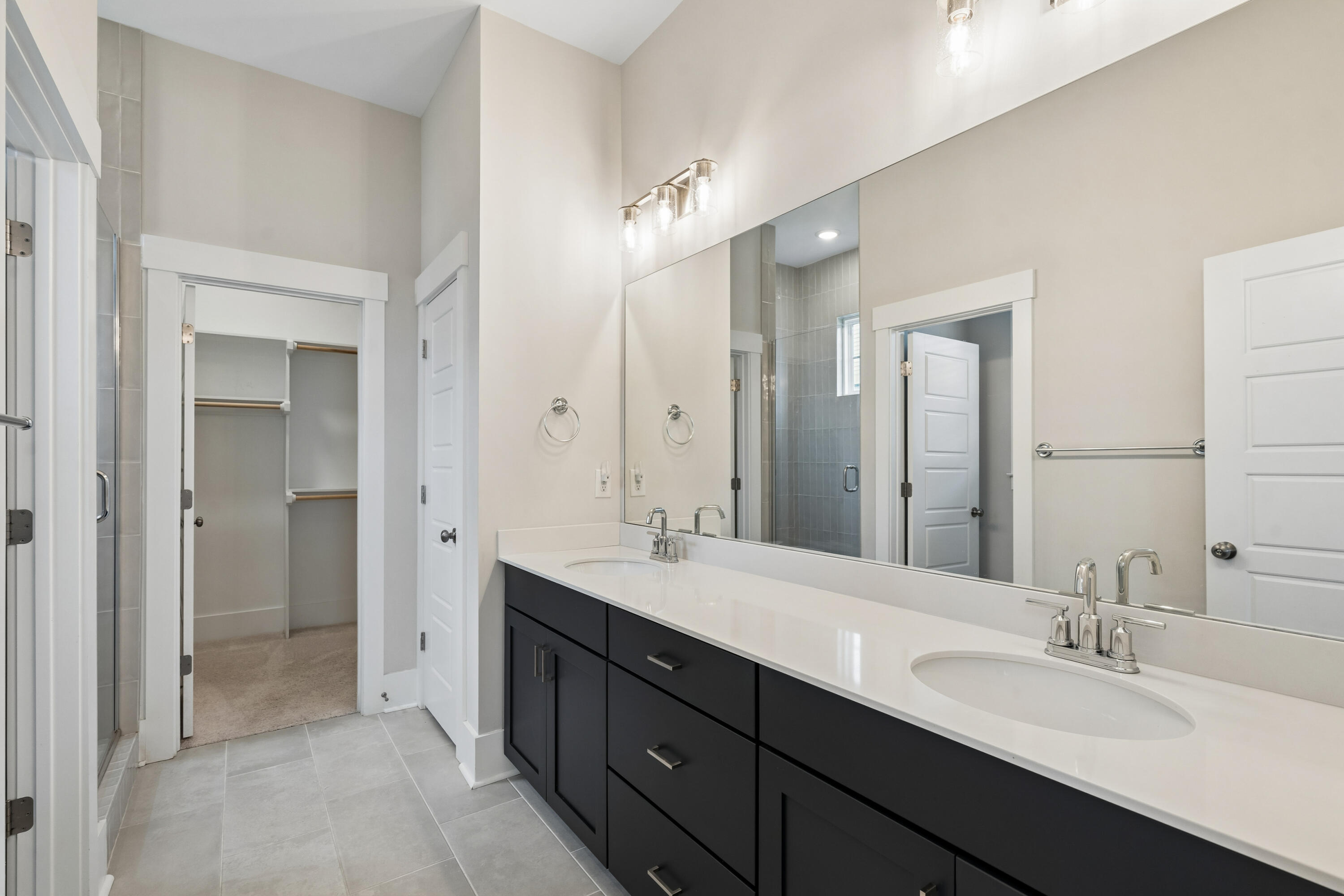 Bathroom with a long double-sink vanity, large mirror, tiled shower, and open walk-in closet.