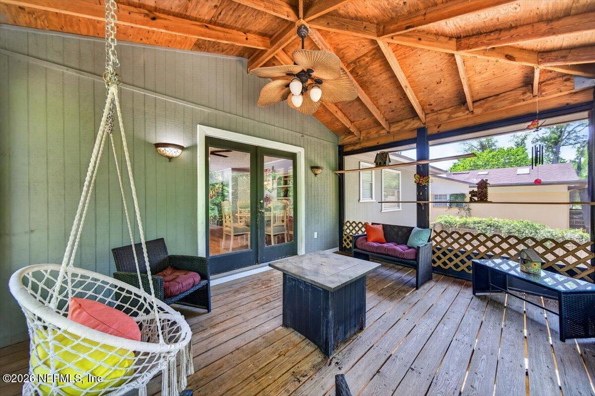 Covered wooden porch with exposed beams, wicker seating, and a hanging swing chair.