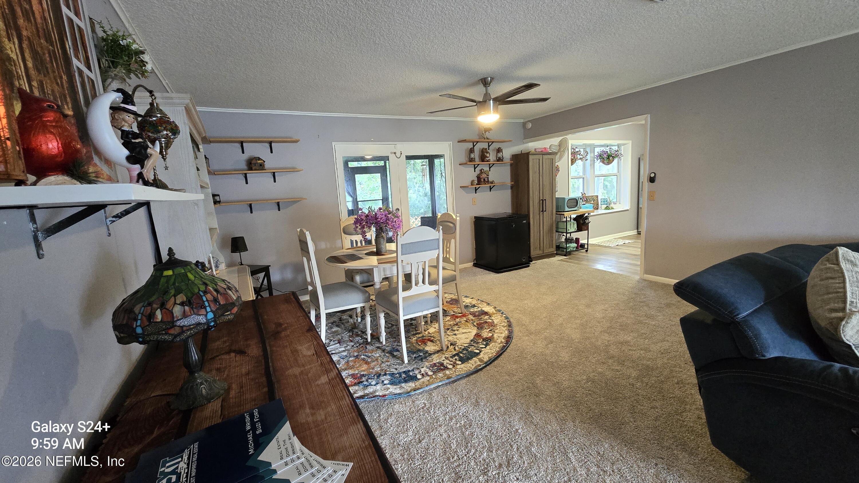 Furnished living and dining area with a round table, patterned rug, open shelving, and dark sofa.