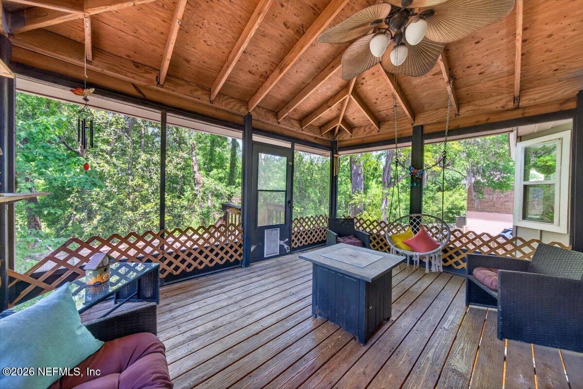 Screened porch with an exposed-wood ceiling, plank flooring, and wicker seating overlooking trees.