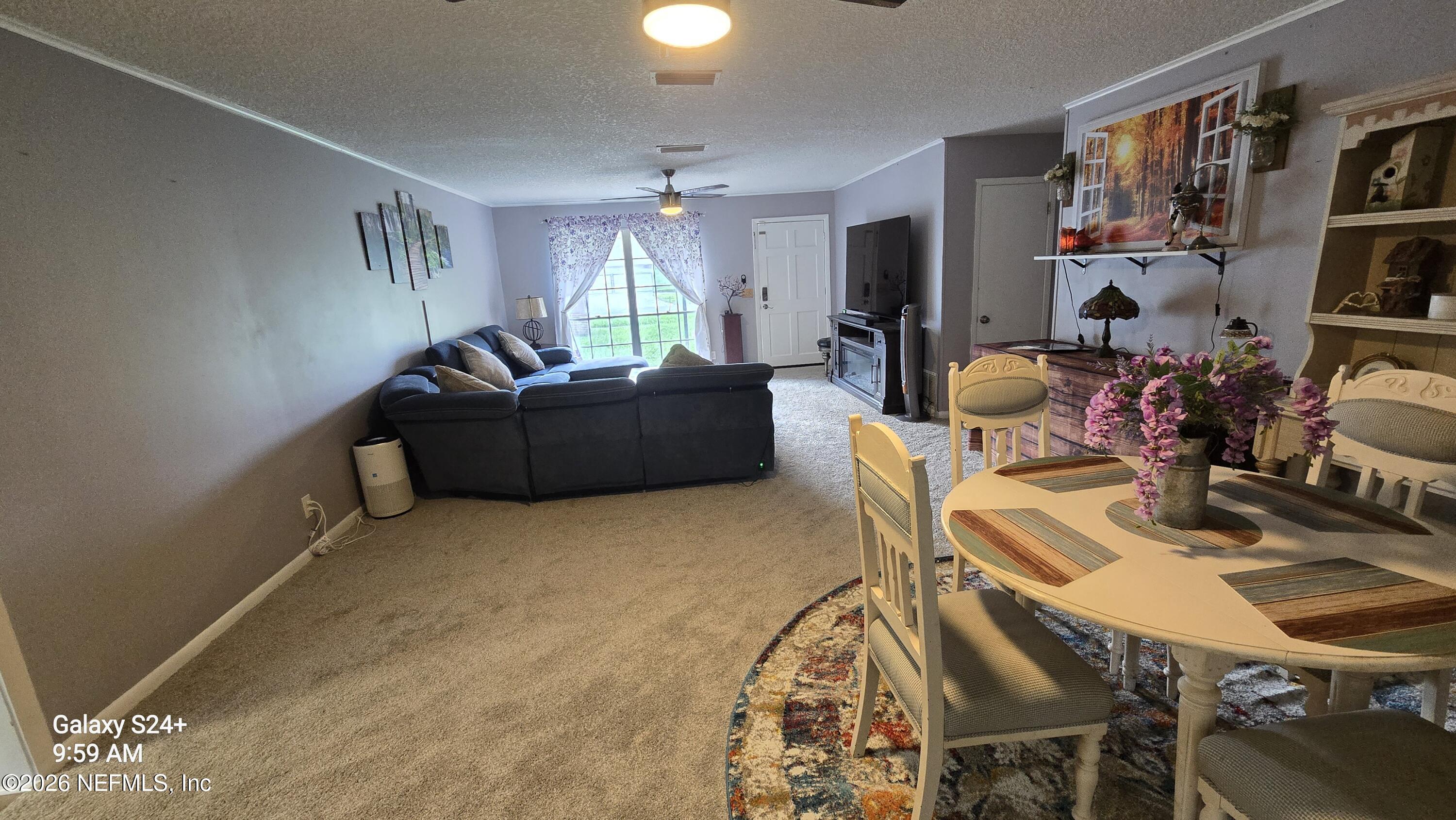 Furnished living and dining room with a dark sectional, curtained window, and dining table with pink flowers.