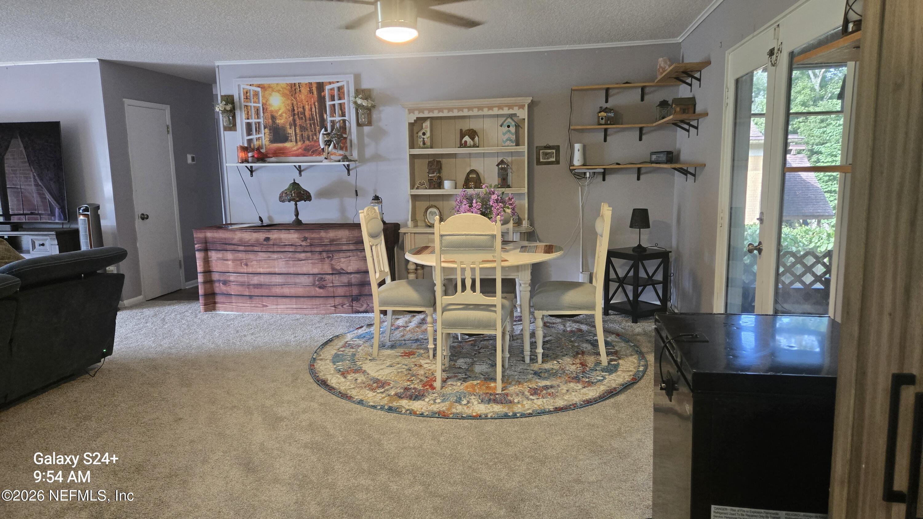 Dining area with a round table, patterned rug, display shelves, and glass patio doors.