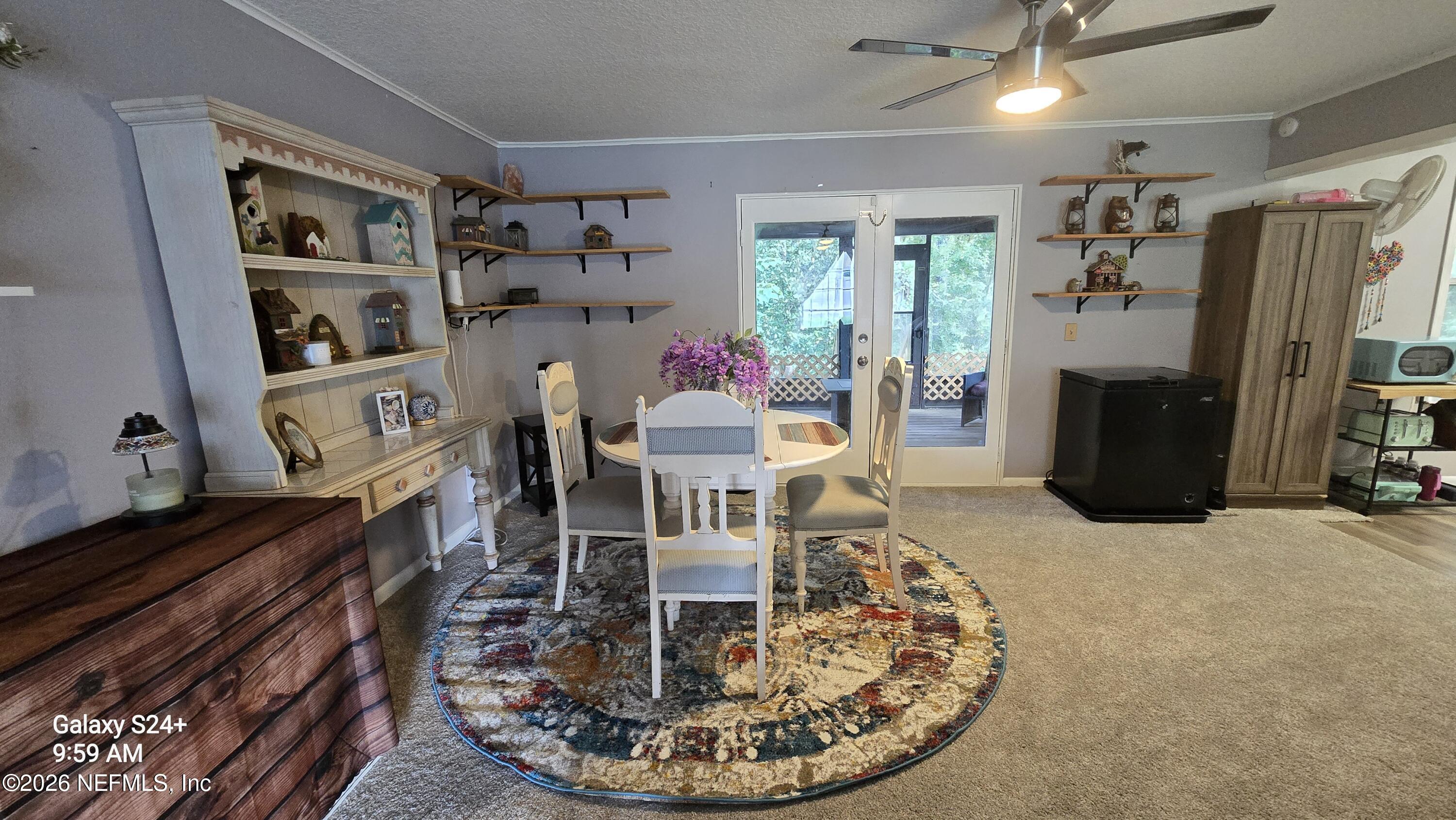 Dining area with a round white table, colorful rug, display shelves, and glass doors to a patio.