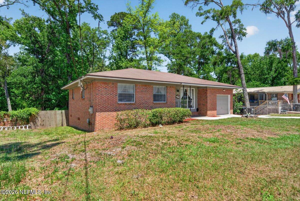 Brick single-story home with an attached garage, front lawn, and mature trees.