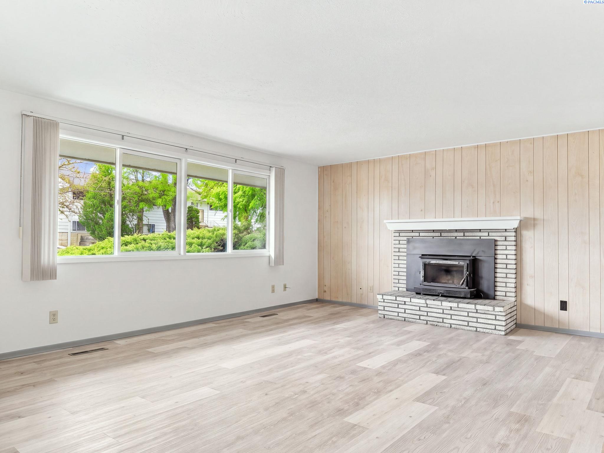 Main level living room with a brick fireplace, a wood paneled wall and a row of windows