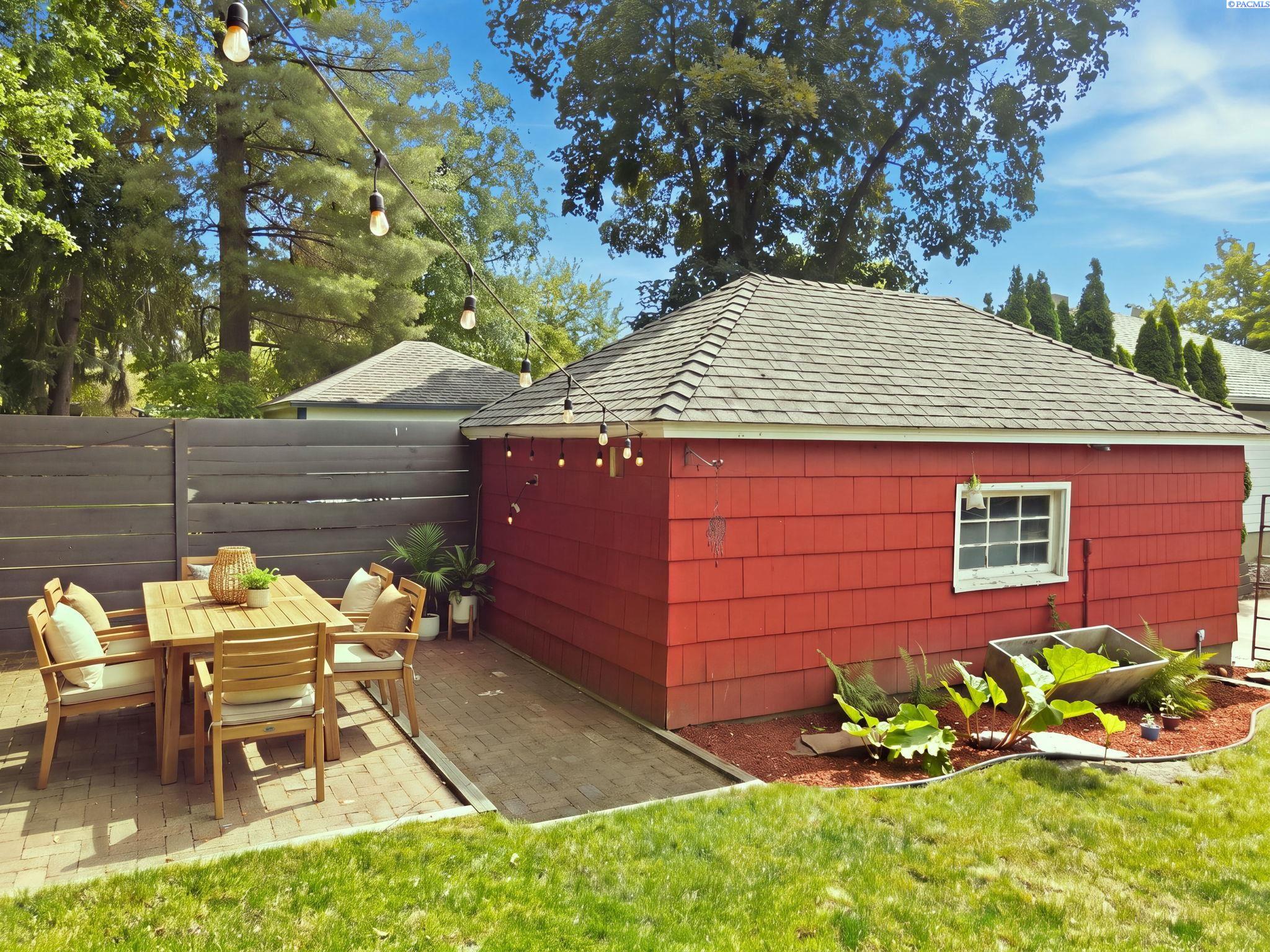 Outdoor dining table on a patio beside the red detached garage