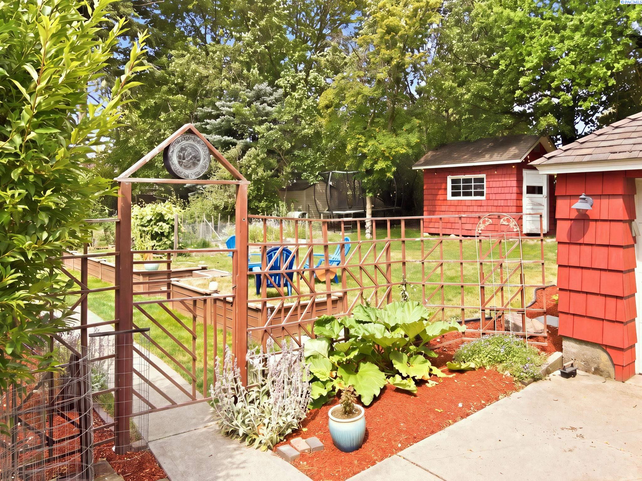 Garden arbor and fence leading into a backyard with a garden bed and red shed