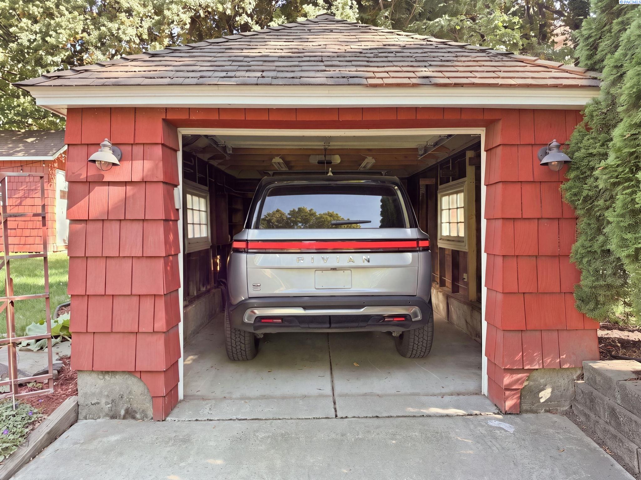 Detached garage with a red shingled front and a full size SUV parked inside