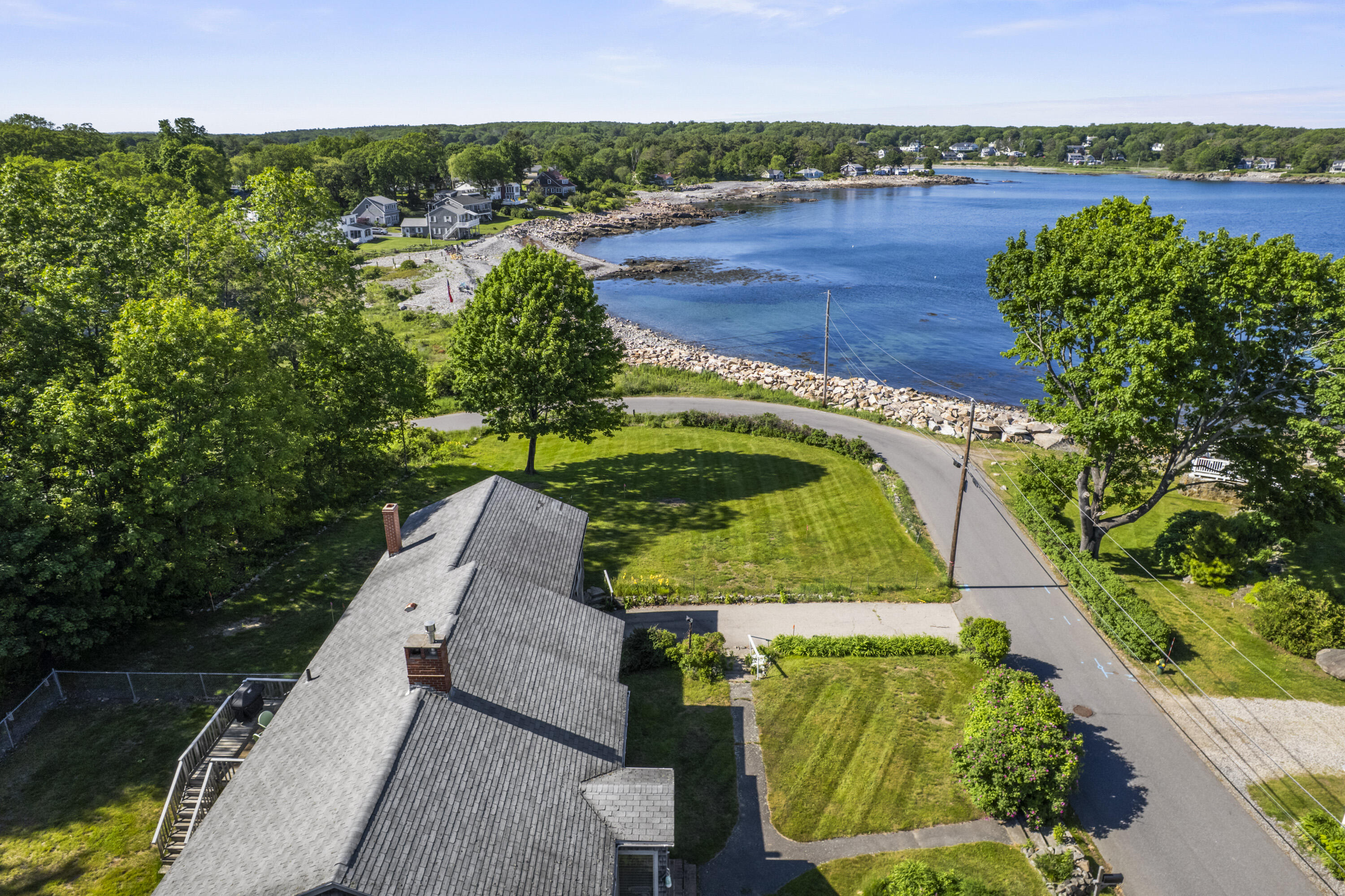 Coastal home beside a rocky shoreline, with a broad lawn and blue bay beyond.