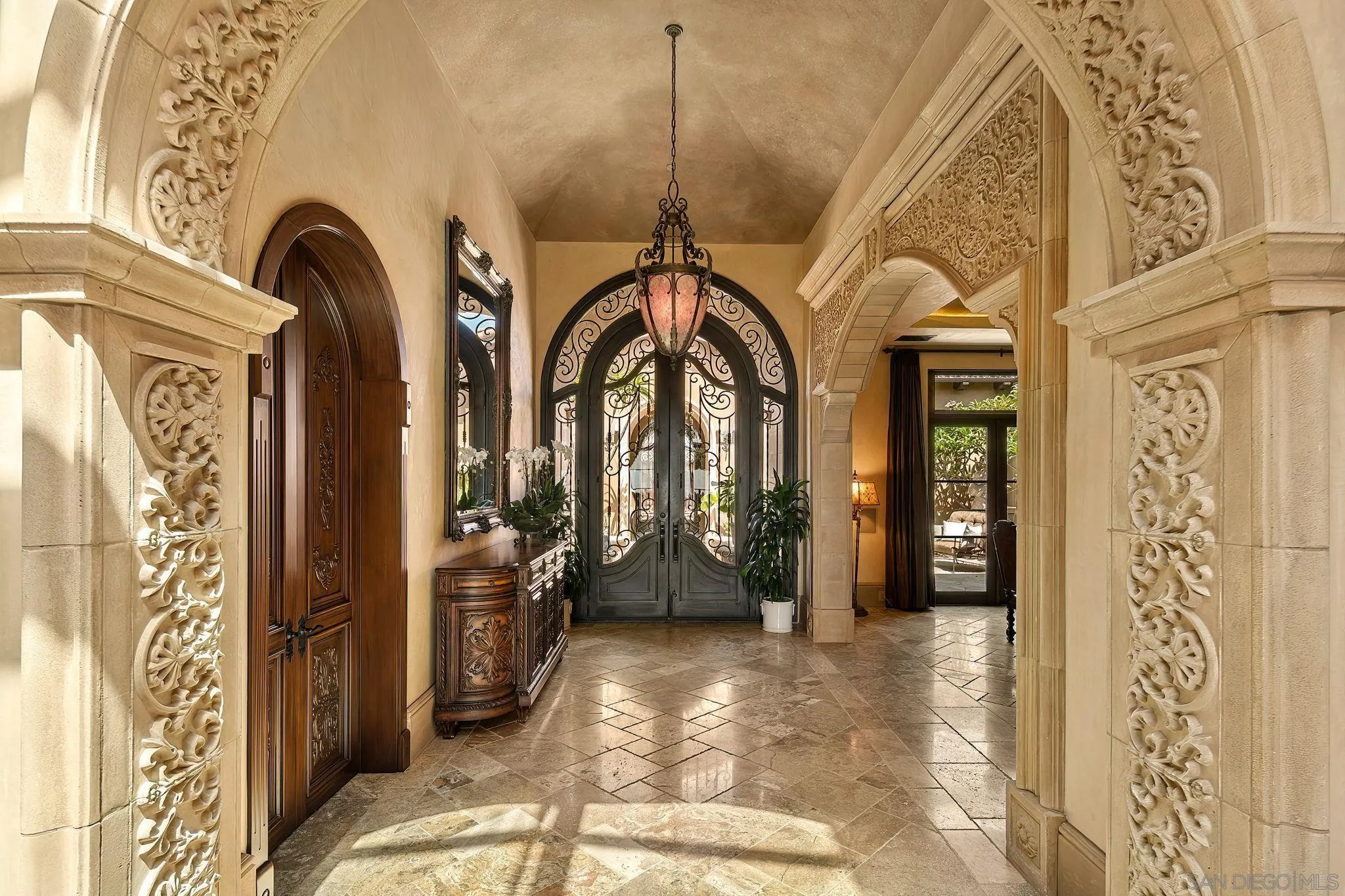 Grand entry foyer with ornate carved arches, wrought-iron glass doors, and a hanging lantern.