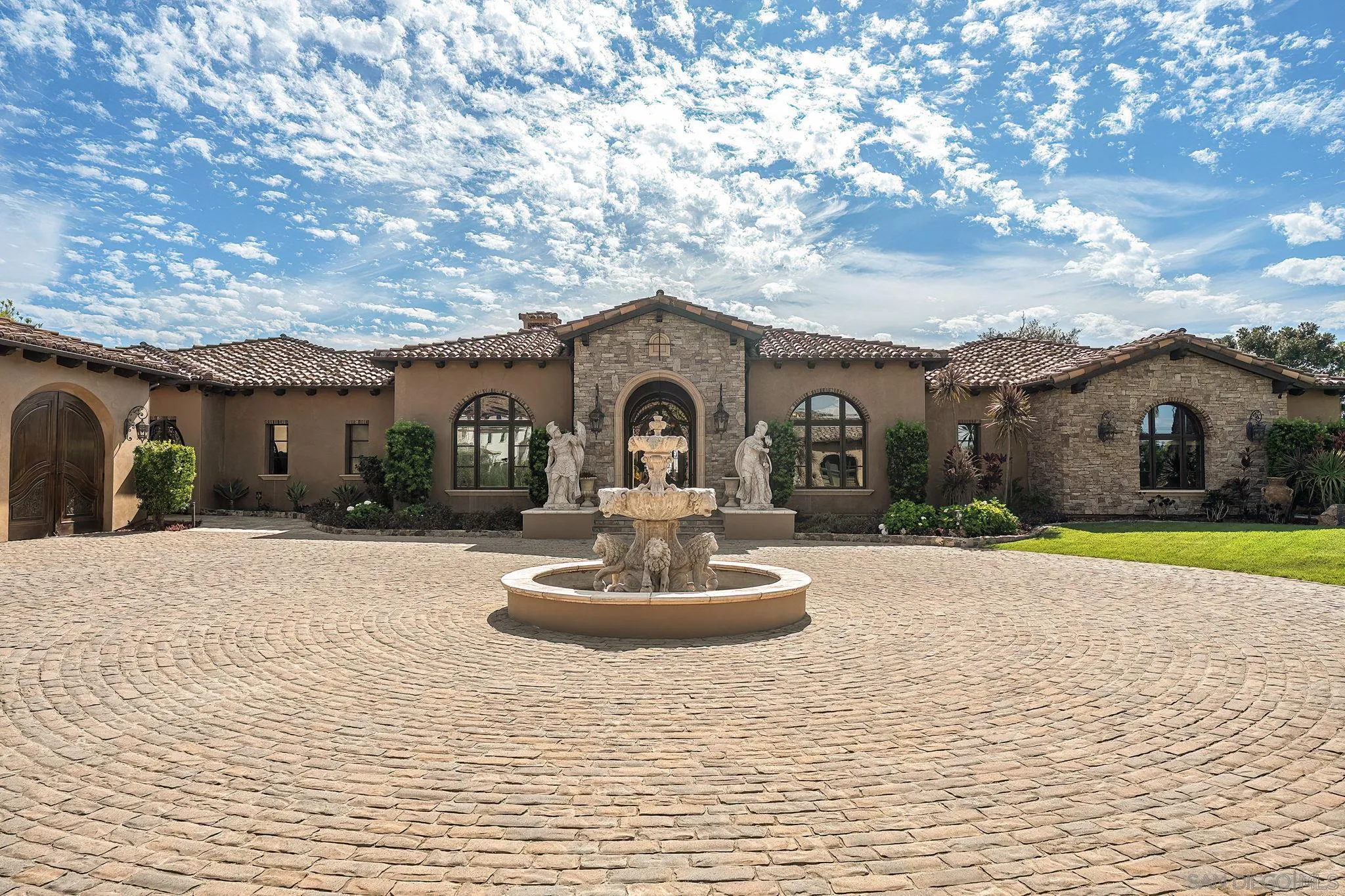Mediterranean-style home with a central fountain in a circular cobblestone courtyard.