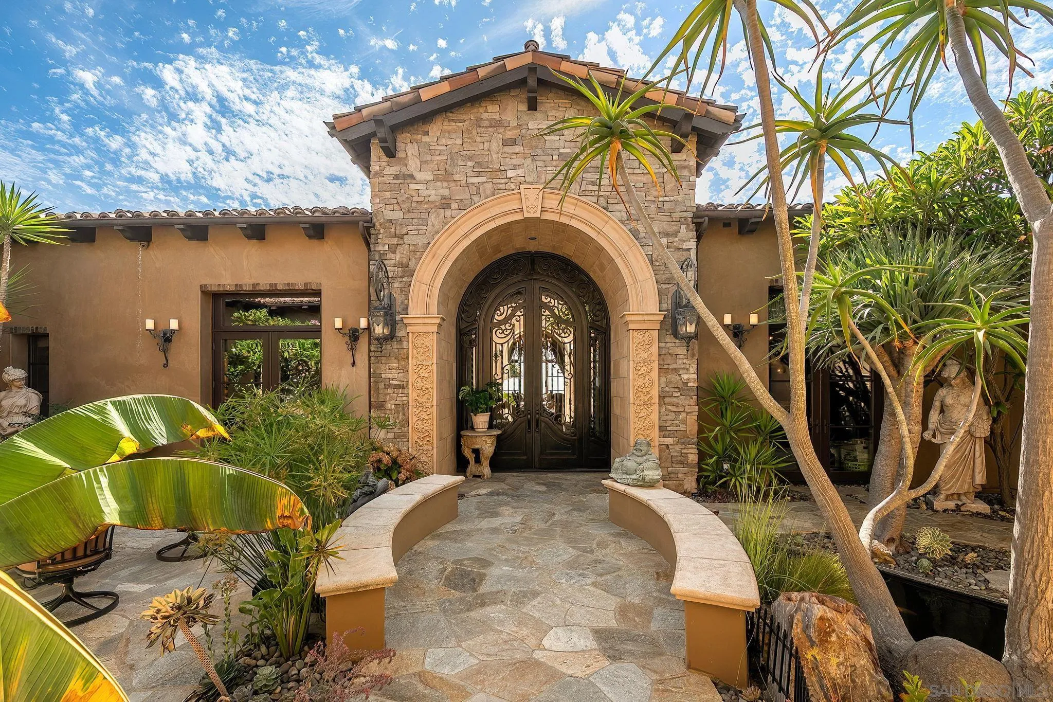 Home entrance with a carved stone arch, ornate iron doors, and tropical landscaping.