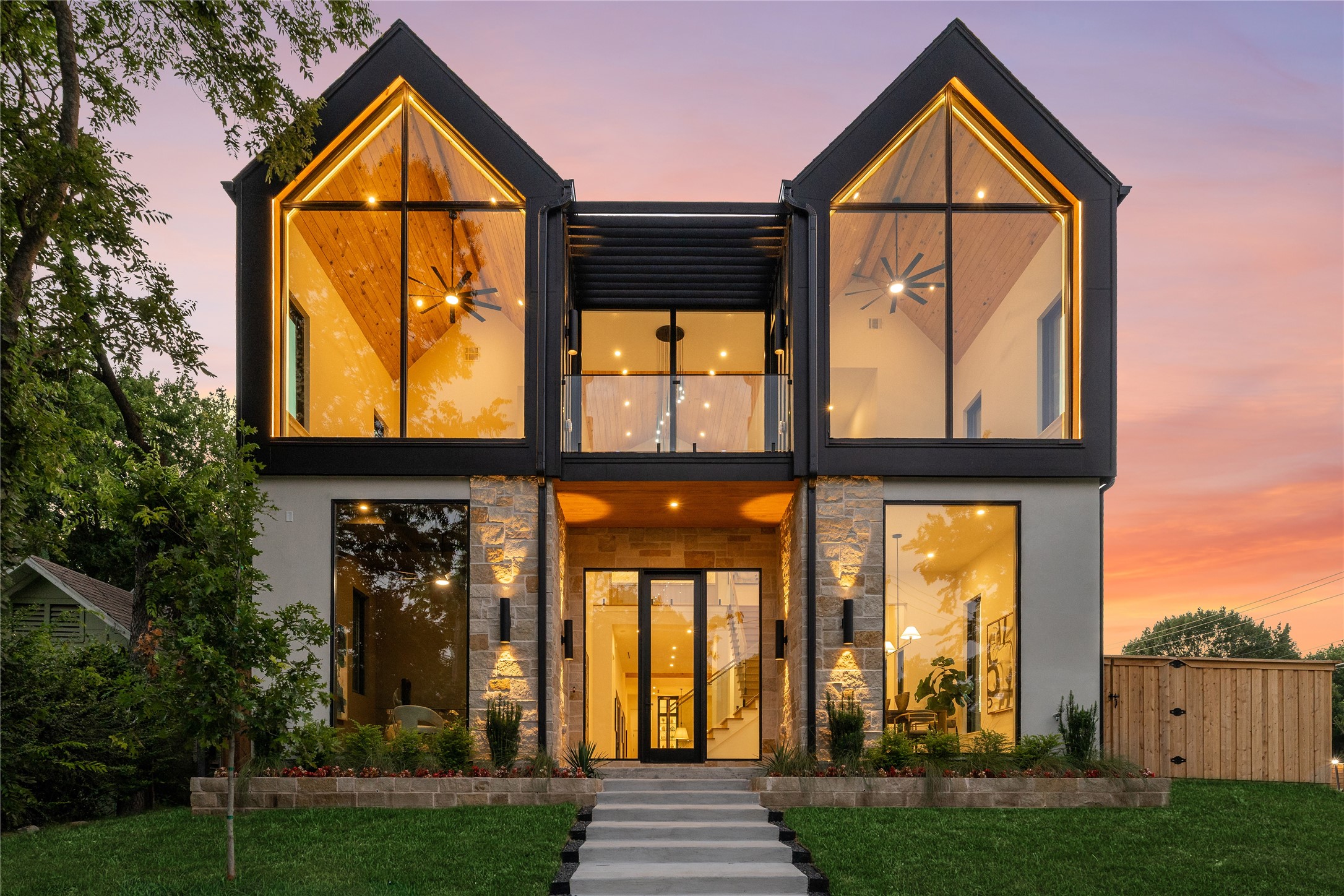 Modern two-story home with paired glass gables and warm lighting at dusk.