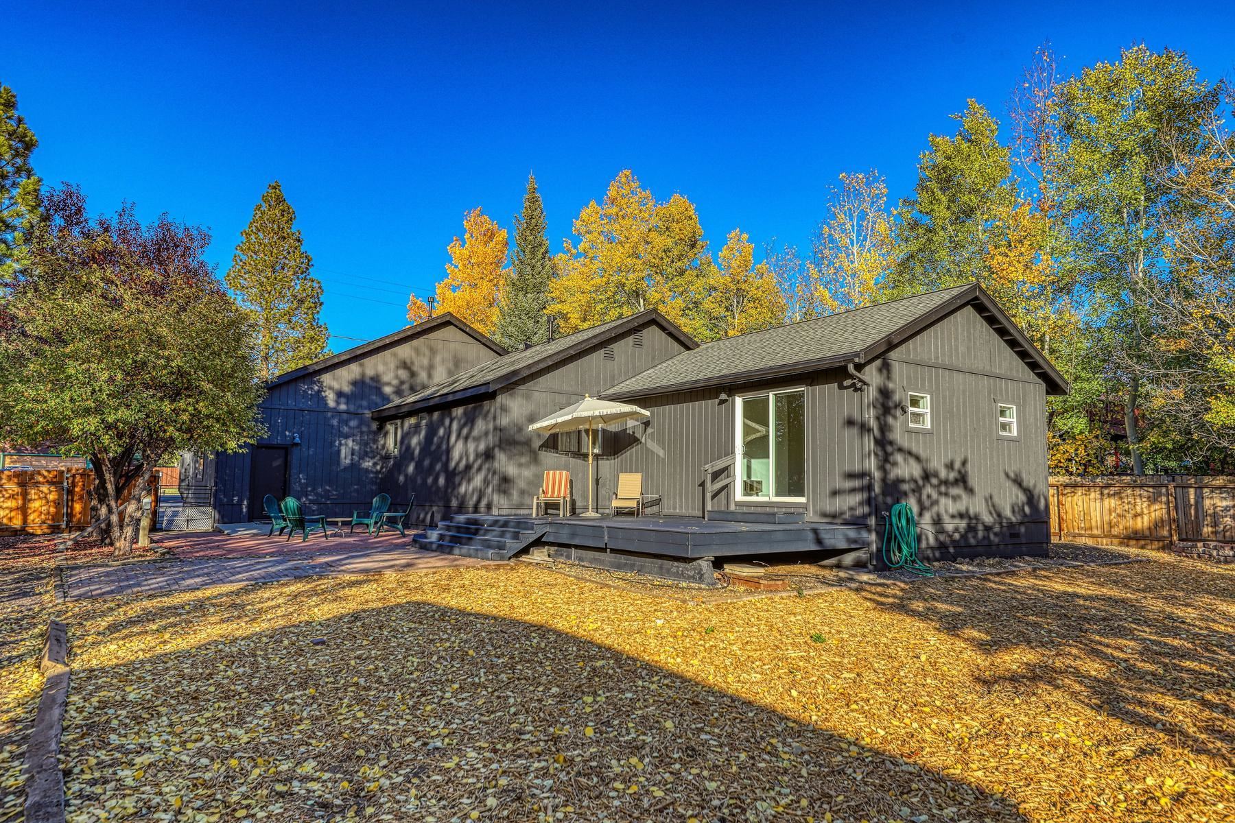 Dark gray home with a raised deck and patio seating beneath autumn trees.