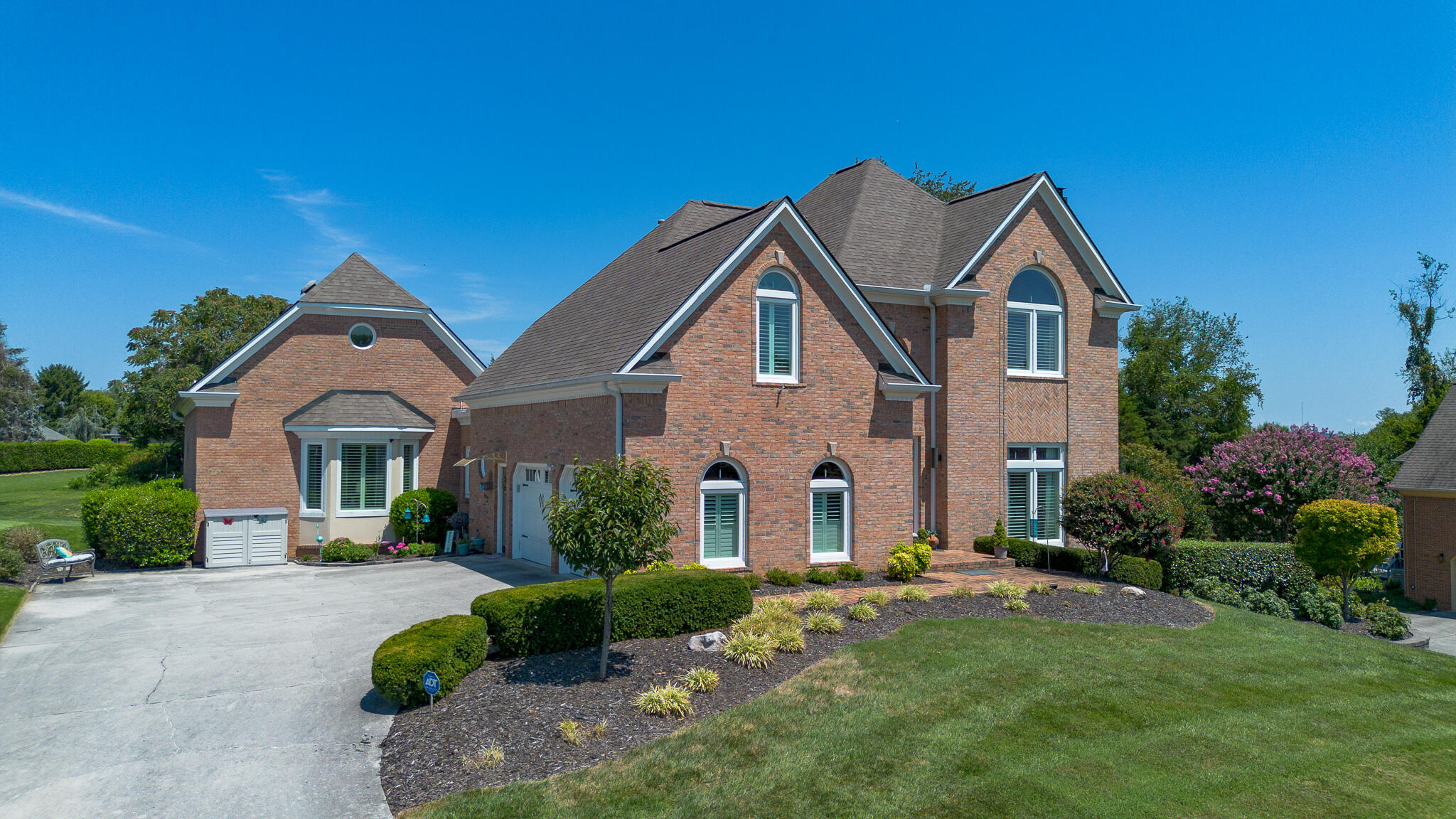 Two-story brick house with steep gabled roofs, arched windows, and landscaped front yard.