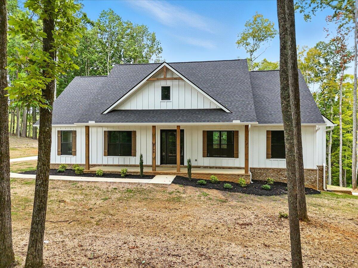 White gabled house with a covered porch, stone foundation, and mature trees in the yard.