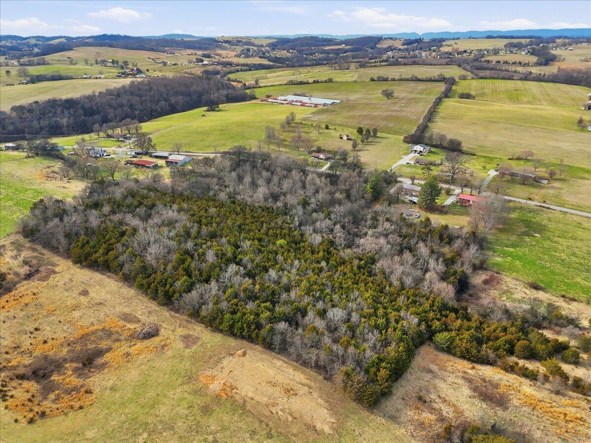 Aerial view of wooded acreage bordered by open fields and scattered rural buildings.