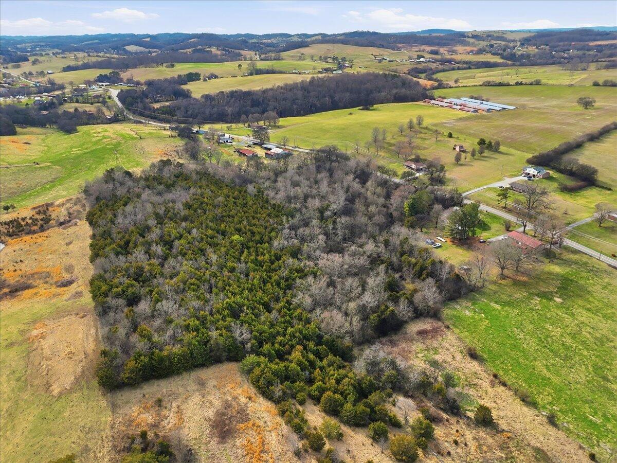 Aerial view of a wooded rural parcel surrounded by open fields and distant rolling hills.