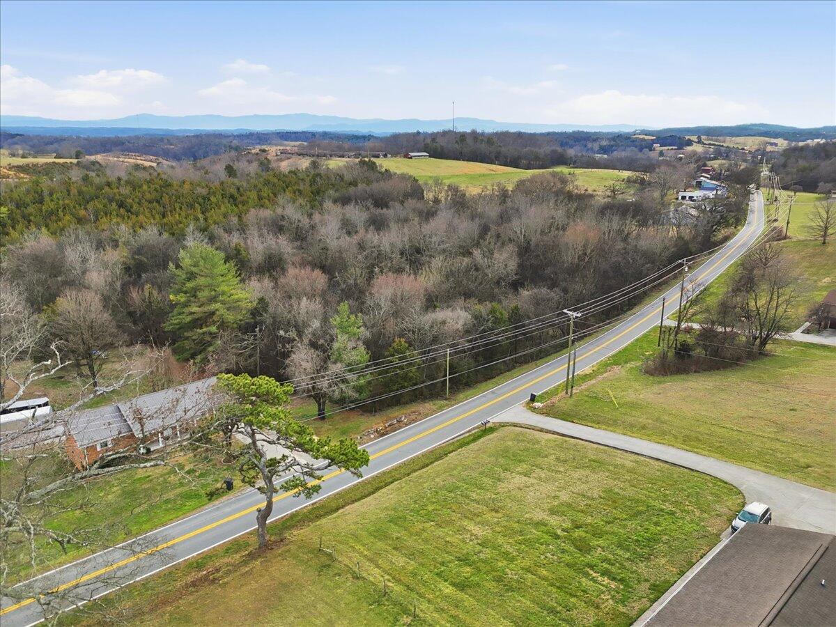Aerial view of grassy property beside a road, with woods and distant mountain ridges.