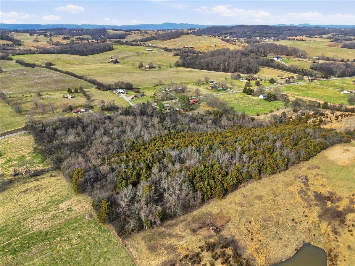 Aerial view of wooded acreage and open fields, with a small pond and distant mountain ridges.