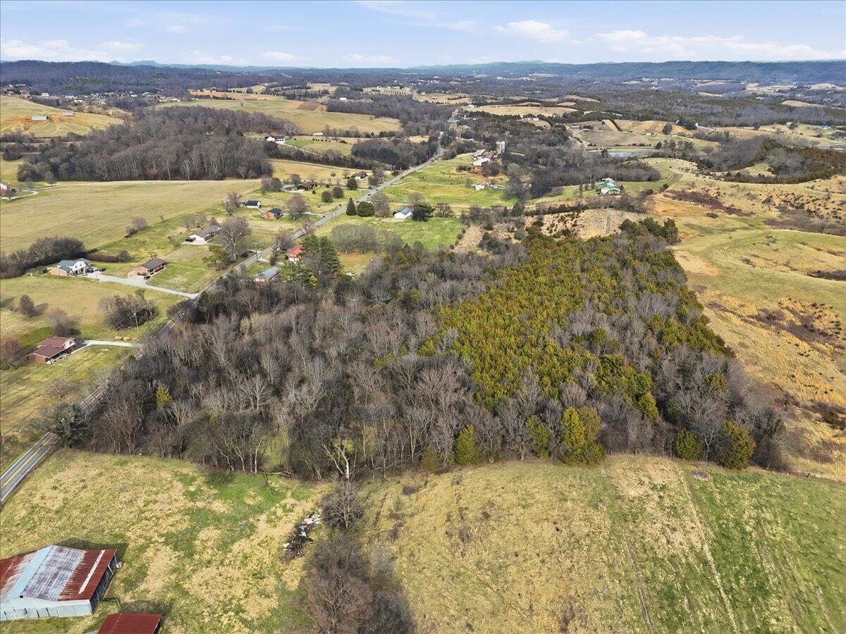 Aerial view of wooded rural land surrounded by open fields and scattered homes.