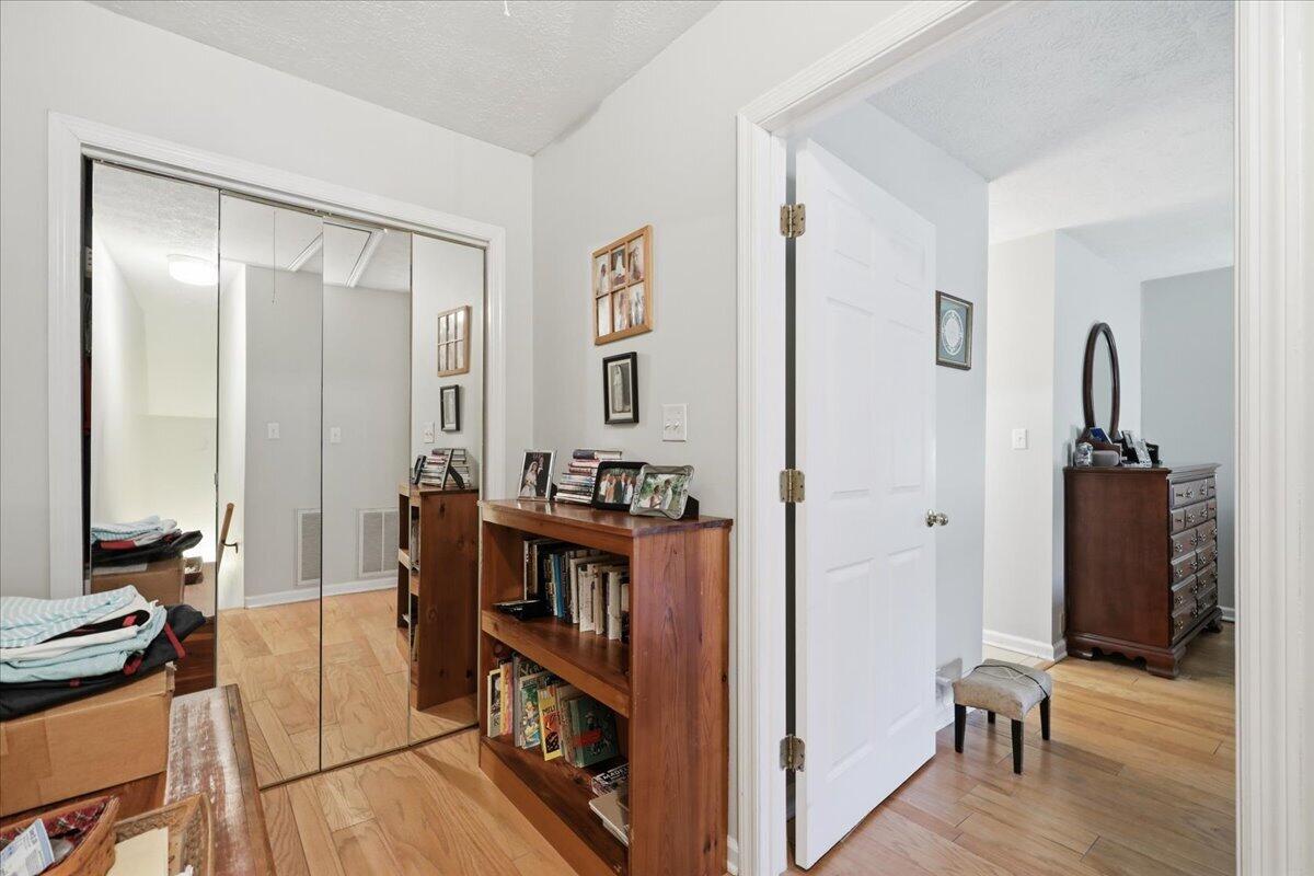 Furnished bedroom with mirrored closet doors, hardwood floors, and a wooden bookcase.